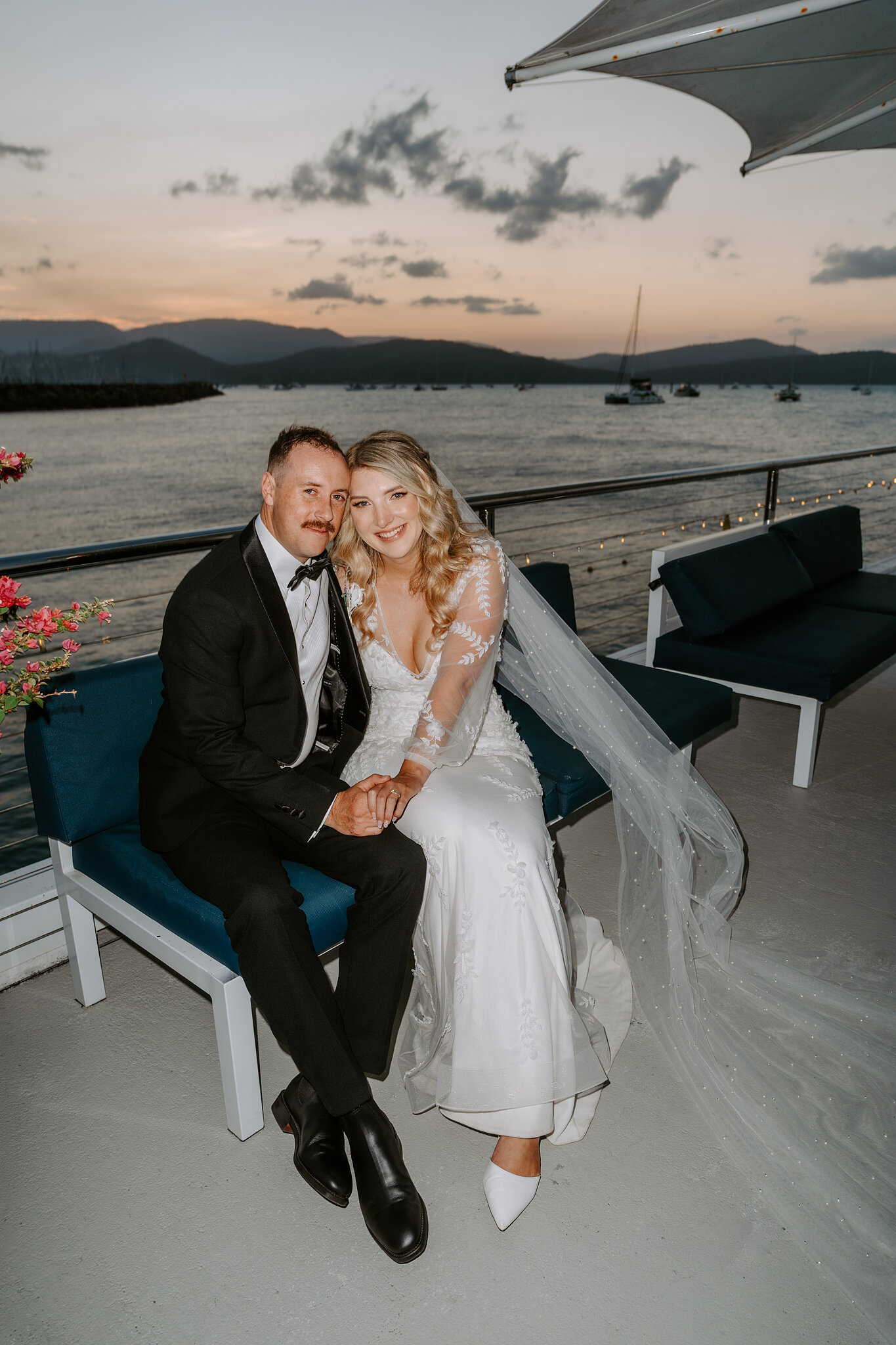 Anna and Brendan on a jetty lounge as the sky turns pink over the Whitsunday hills.