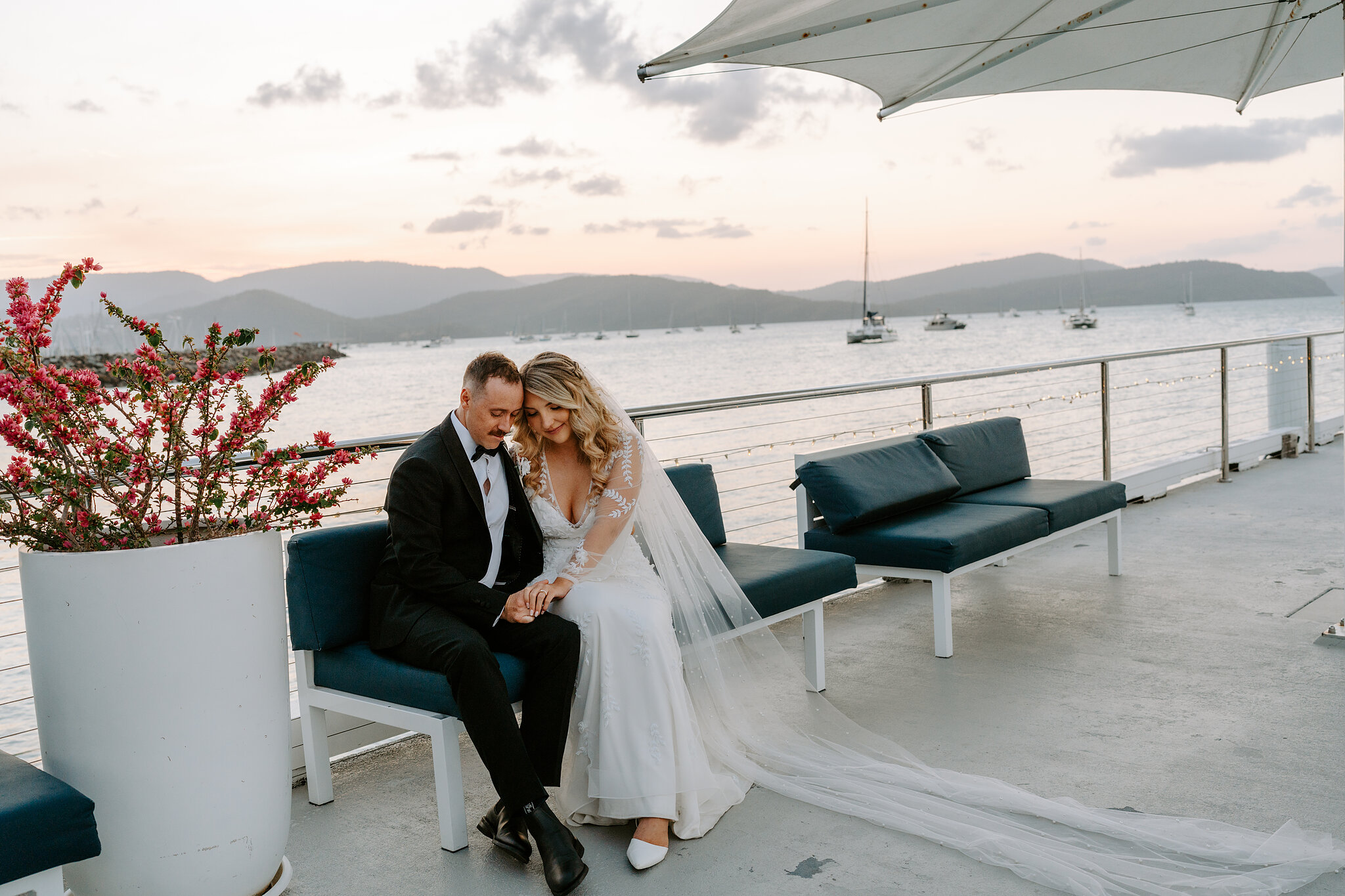 Anna rests her head on Brendan’s shoulder on the jetty at dusk, her veil across the deck.