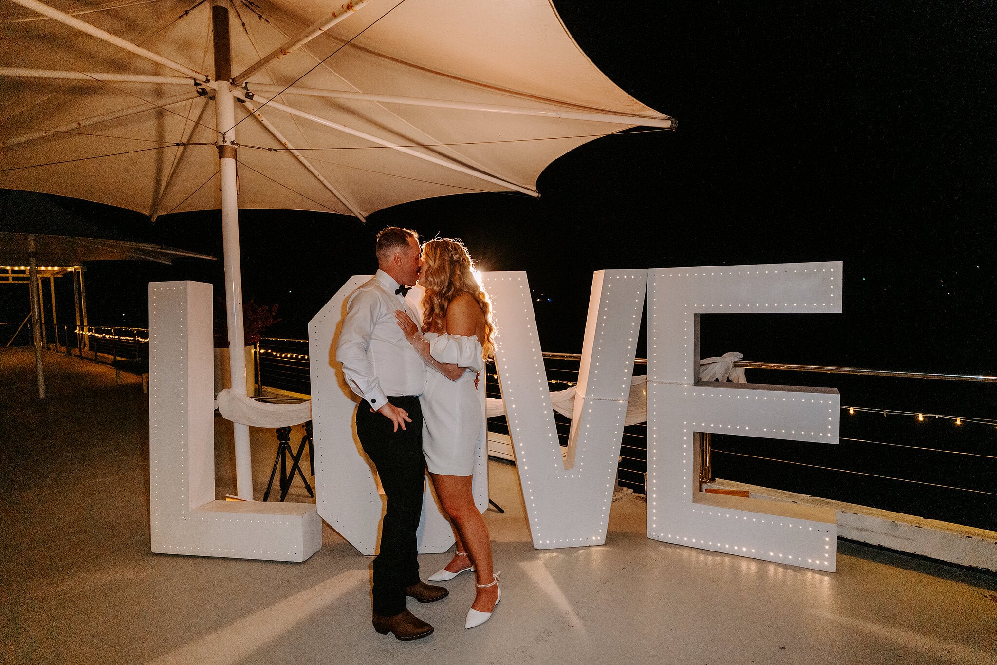 A kiss between the light-up LOVE letters under the shade sails.