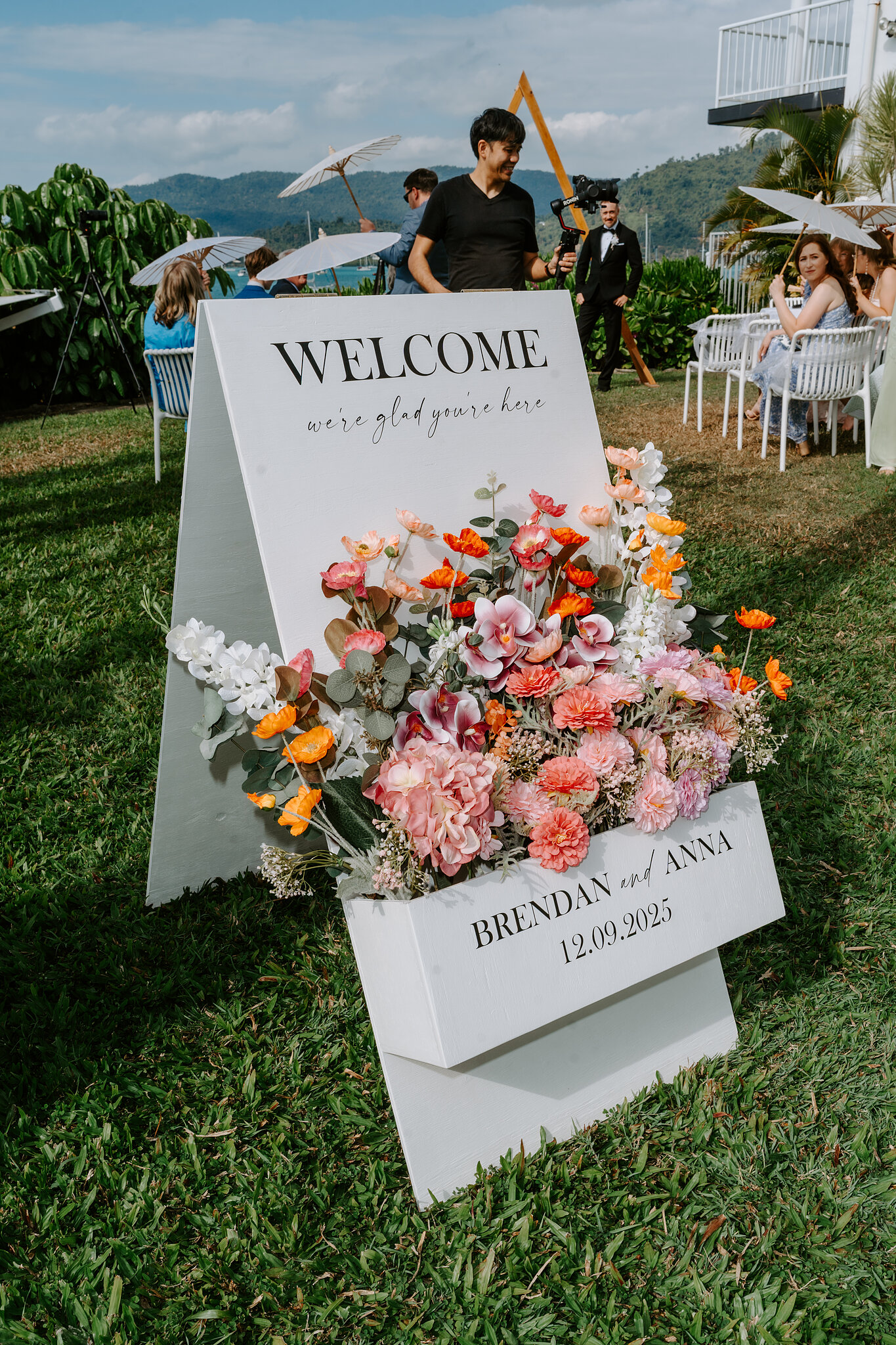 A welcome sign for Brendan and Anna with a burst of pink, coral and white flowers on the Upper Lawn.