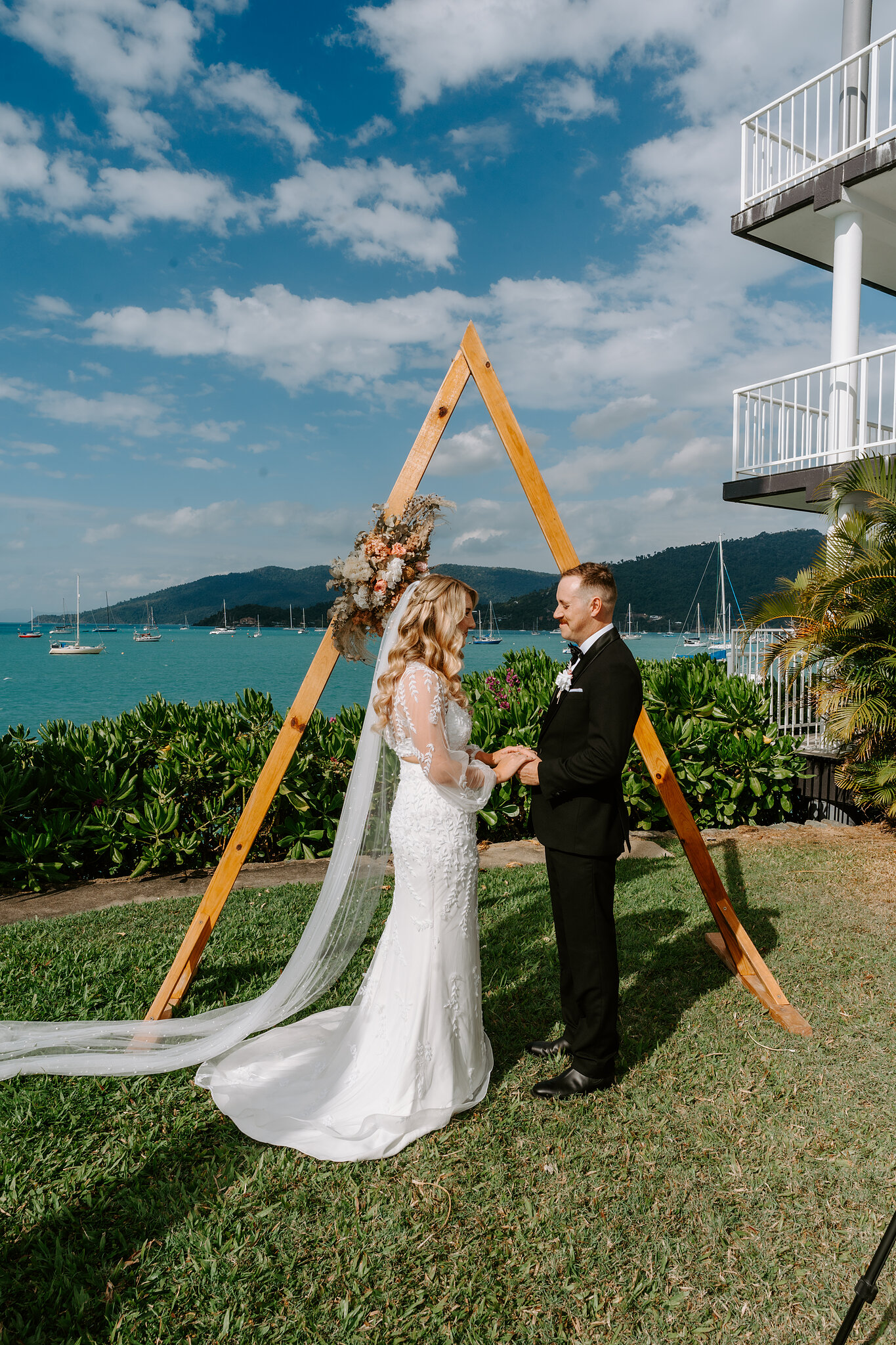 Anna and Brendan hold hands for their vows under the timber arbour on the Upper Lawn at Coral Sea Resort.