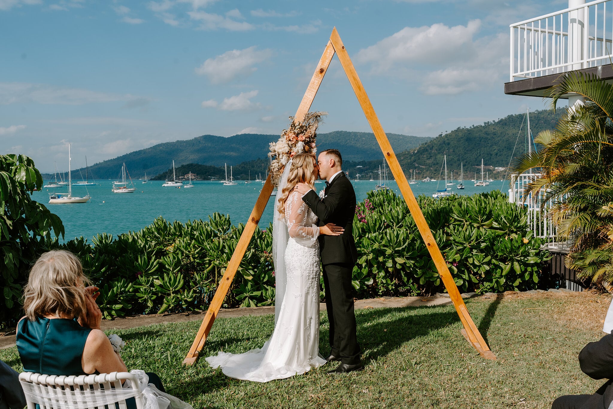 The first kiss under the timber arbour, yachts and Whitsunday hills behind.