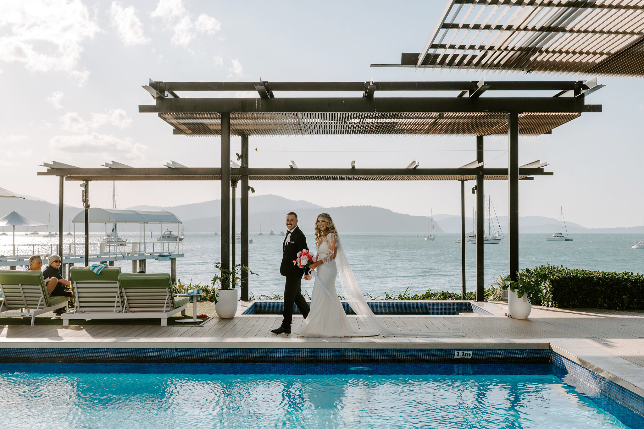 Anna and Brendan walk beneath the pergola by the pool at Coral Sea Resort.