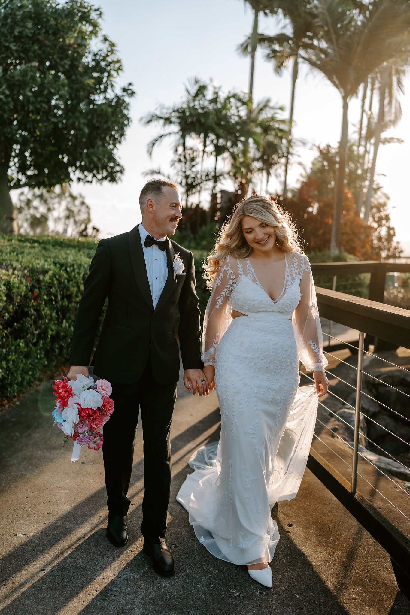 Anna and Brendan walk hand in hand along a palm-lined path at Coral Sea Resort.