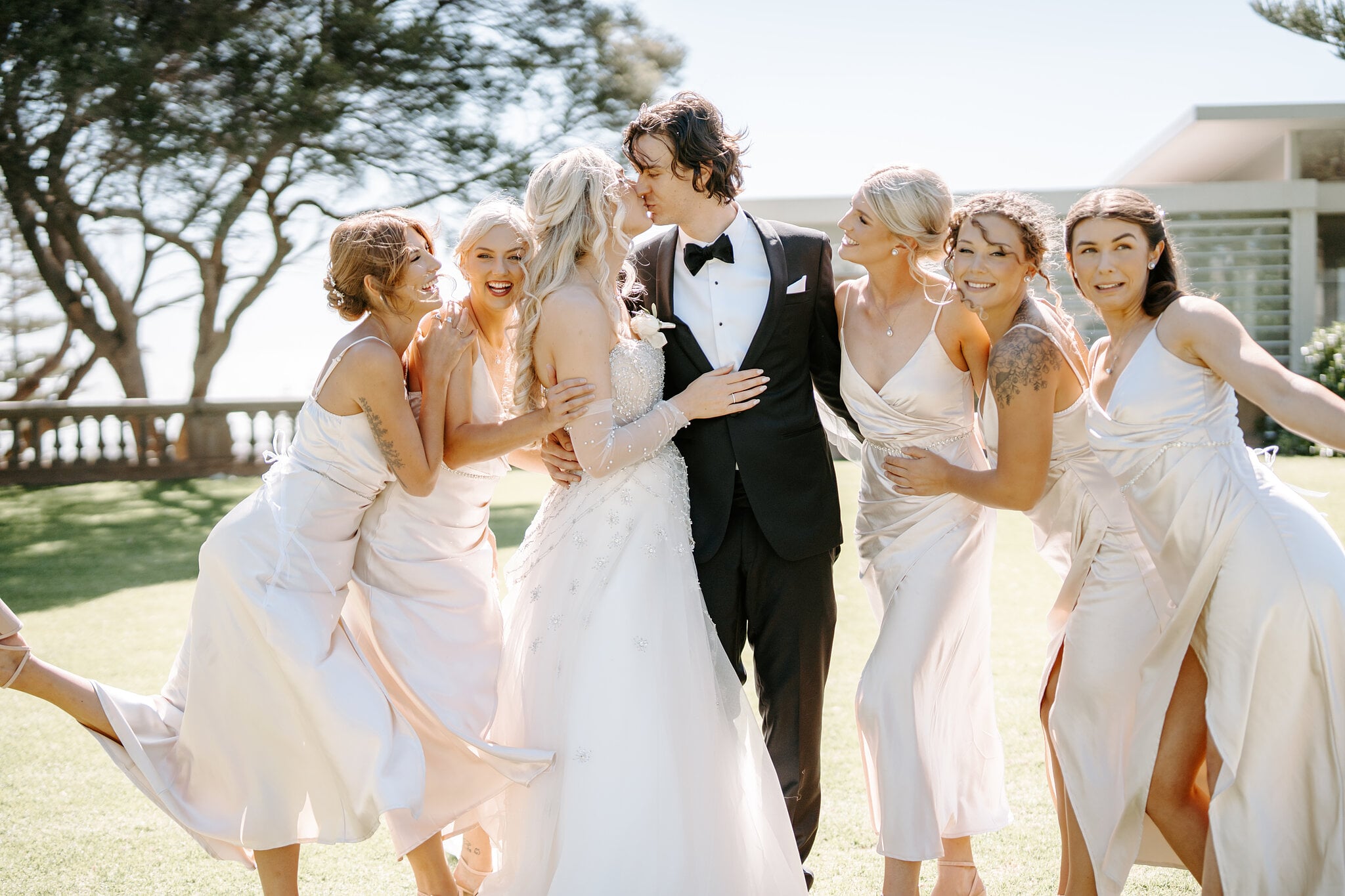 The bridesmaids pile in around Claire and George for a kiss on the lawn at Cottesloe Civic Centre.