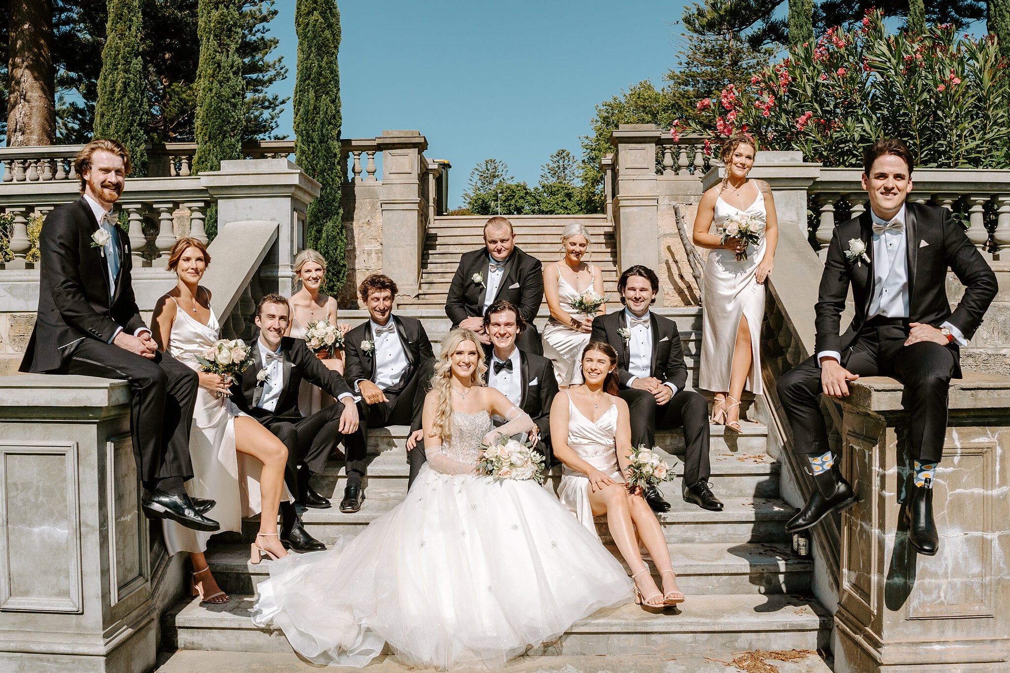 The whole bridal party sprawls across the stone stairs and balustrade at Cottesloe Civic Centre.