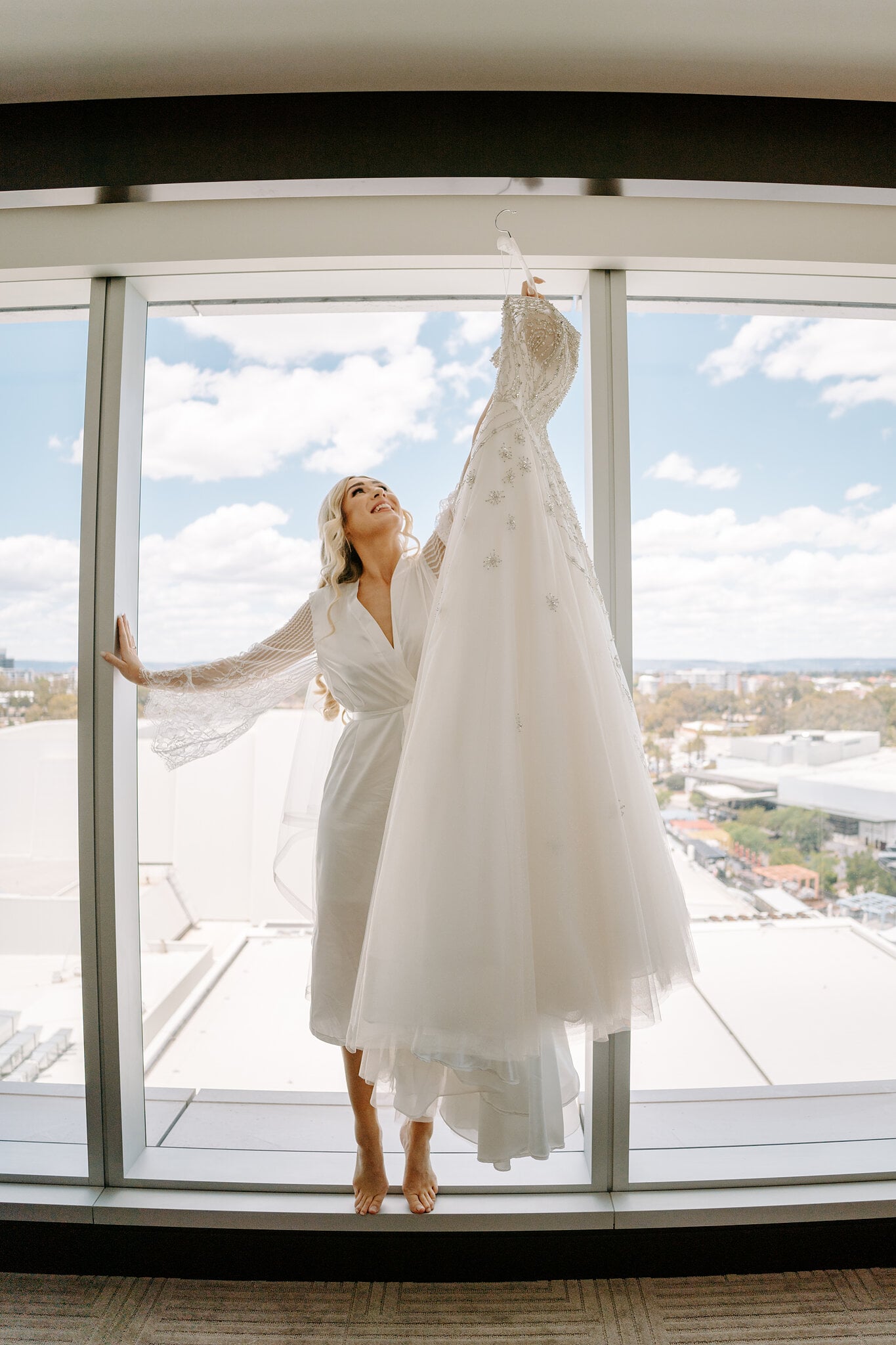 Barefoot in her robe, Claire reaches up to her ballgown hanging against the floor-to-ceiling glass.
