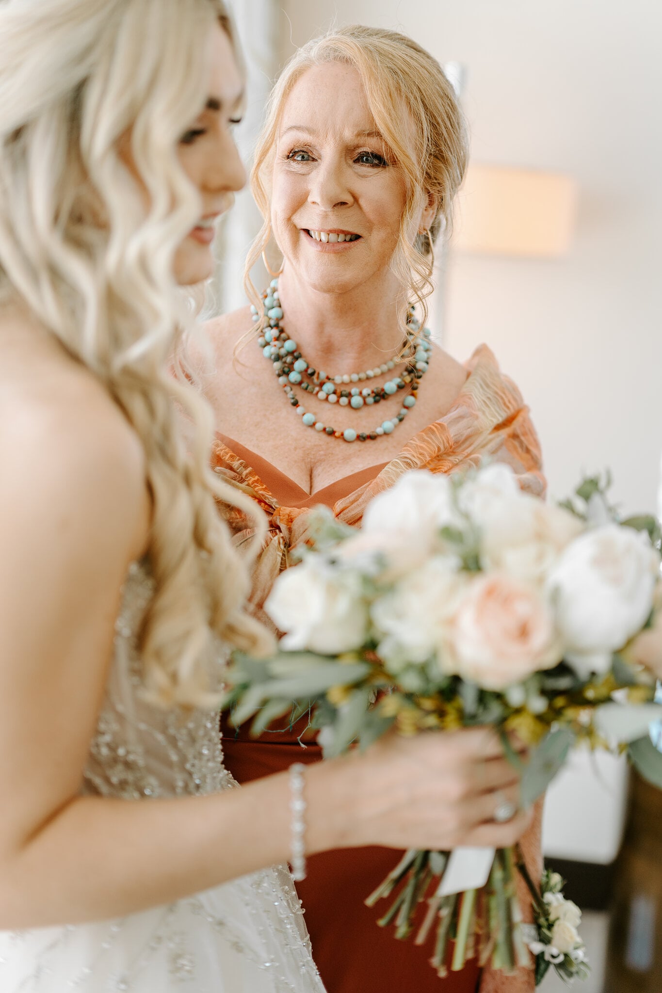 Claire’s mum, in a burnt orange gown and turquoise beads, smiles at Claire and her bouquet.