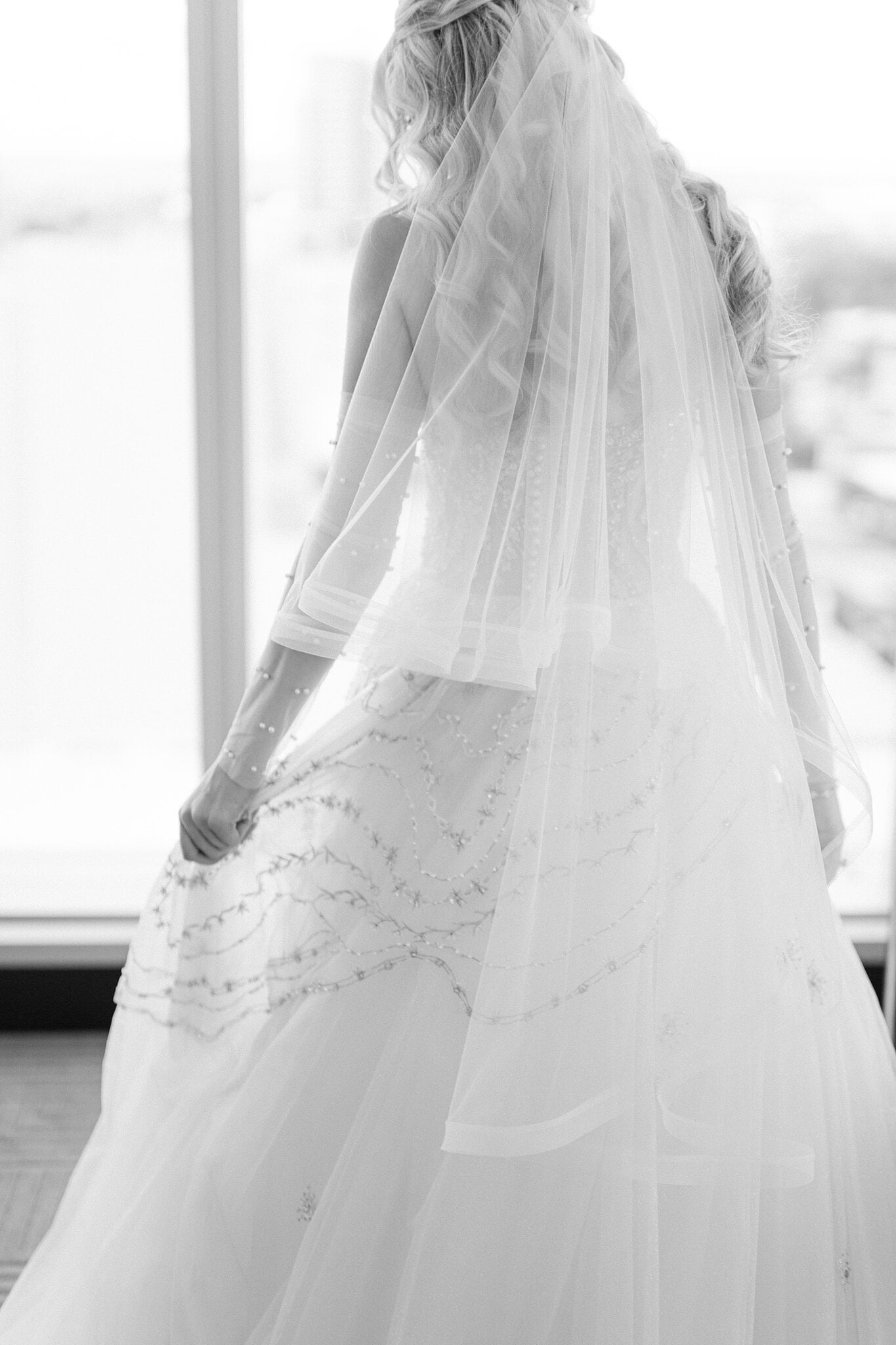 Black and white of Claire from behind, her veil falling over the beaded ballgown by the window.