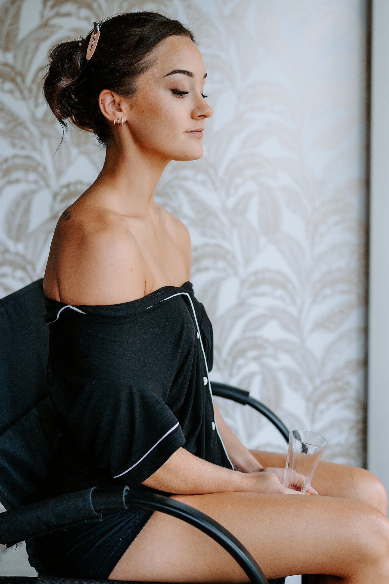 Emma sits by a palm-print wall in black satin pyjamas, hair already pinned up.