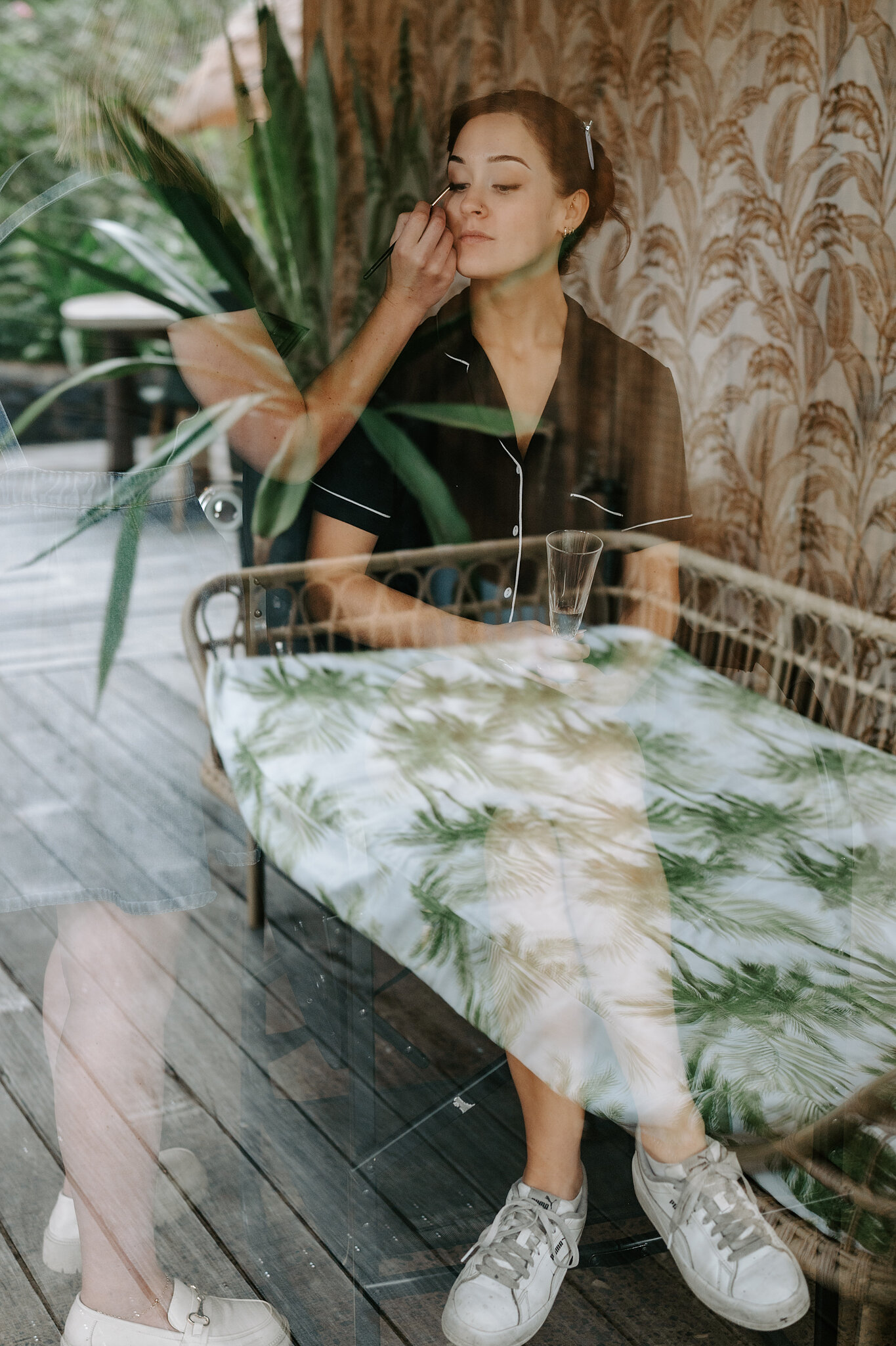 Emma does her own make-up on the deck, reflected among the palms in the glass.