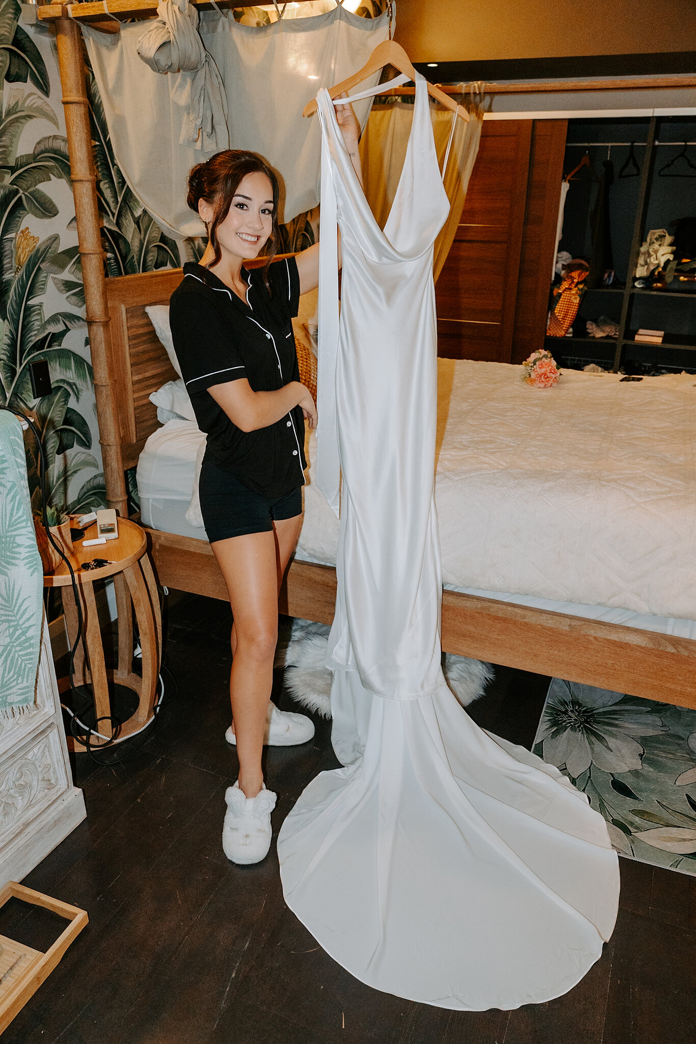 Emma in black pyjamas beside her satin gown hanging from the four-poster bed.