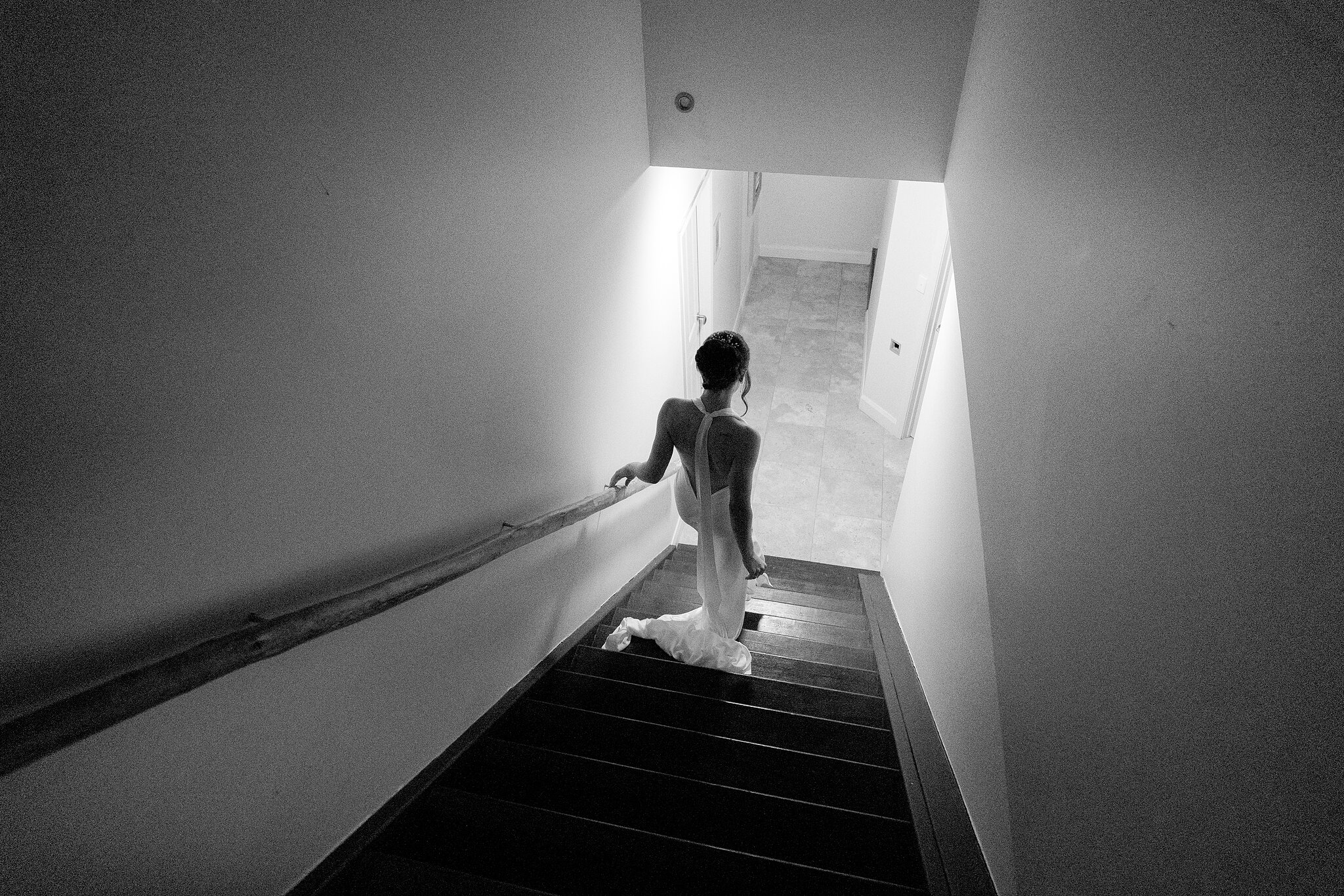 Emma heads down the staircase in black and white, light pouring in below.