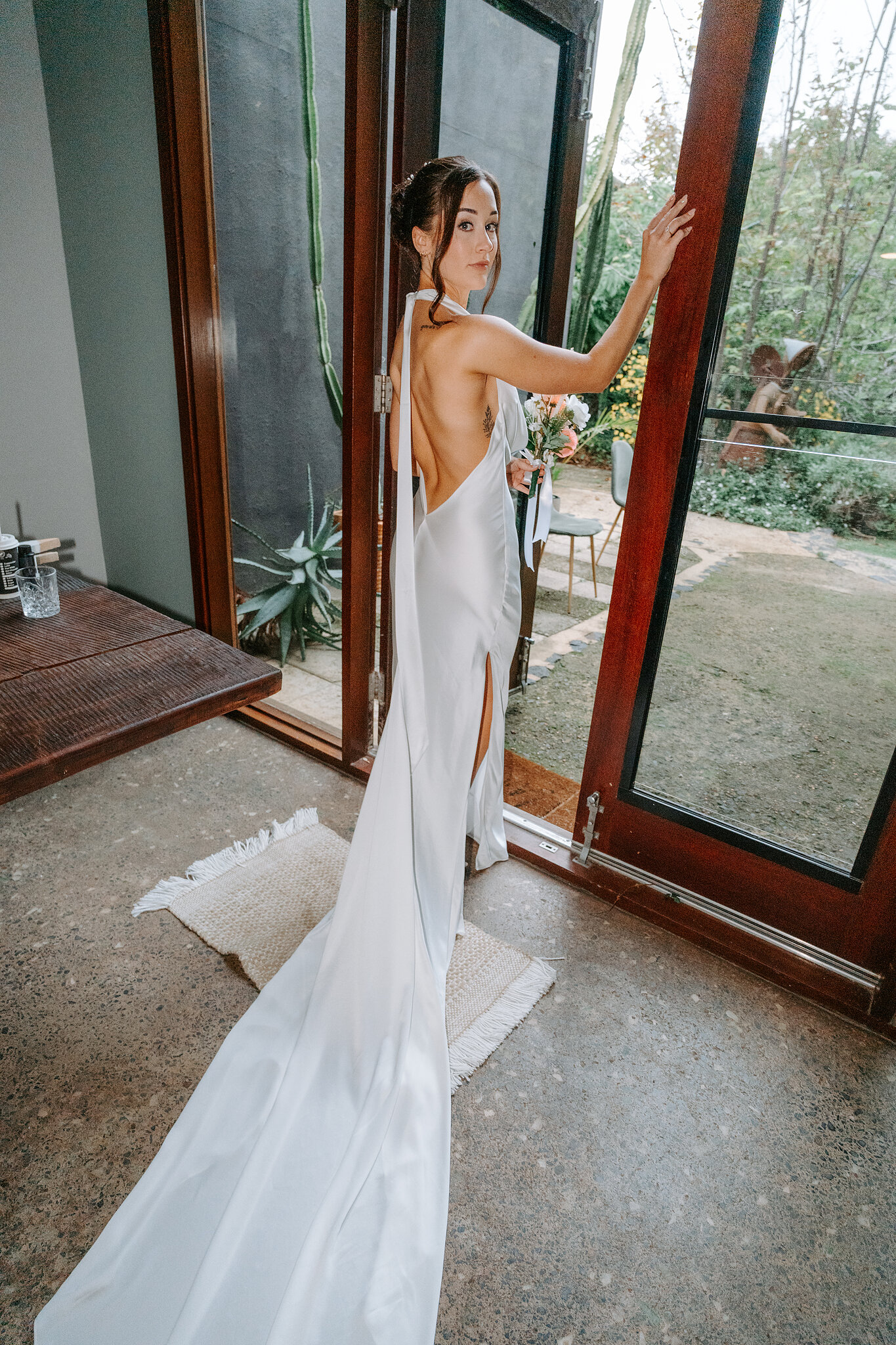 Emma pauses at the open glass doors, her train pooled on the polished concrete floor.