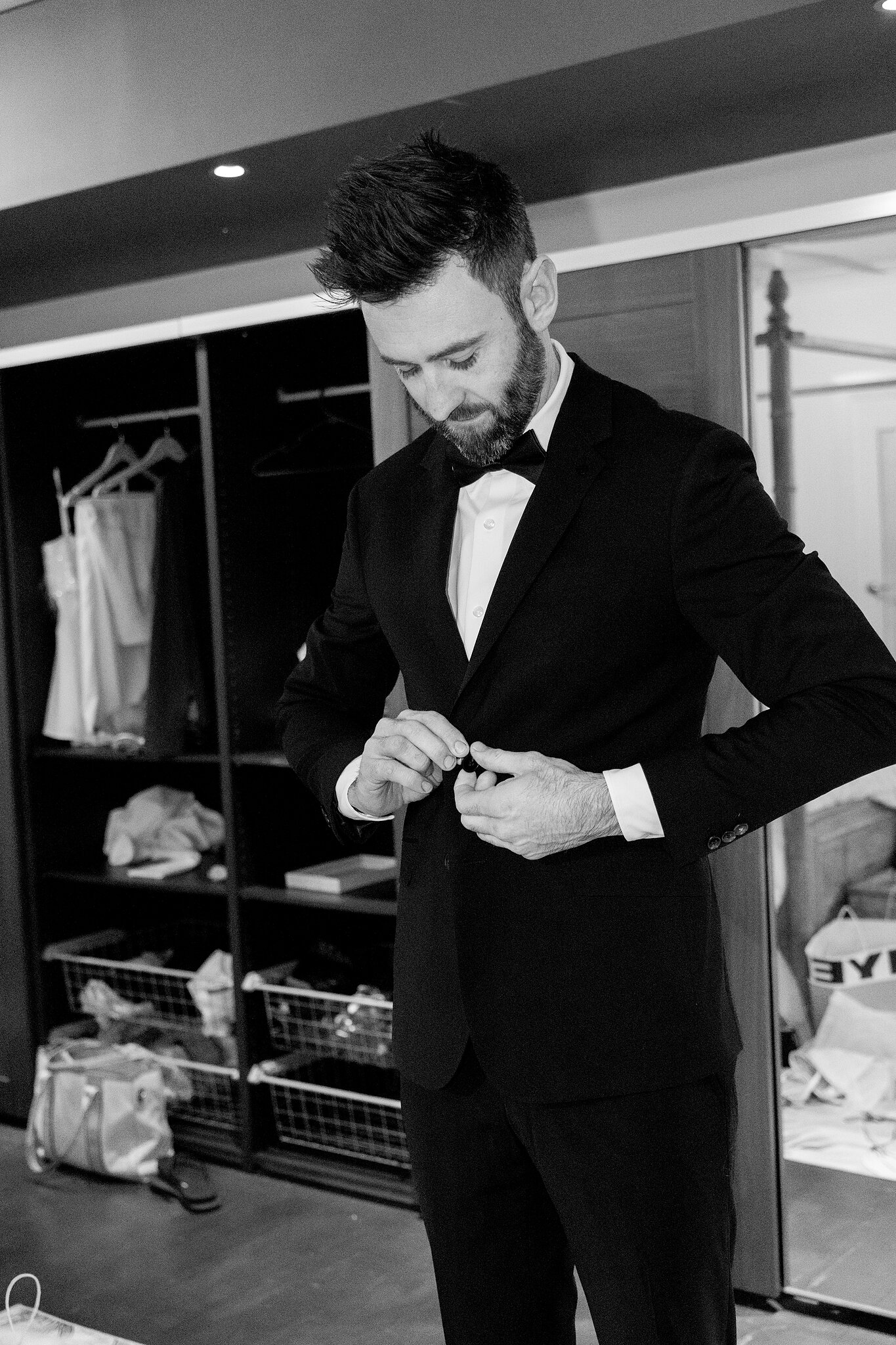 Dave fastens his tuxedo jacket in the wardrobe room, in black and white.