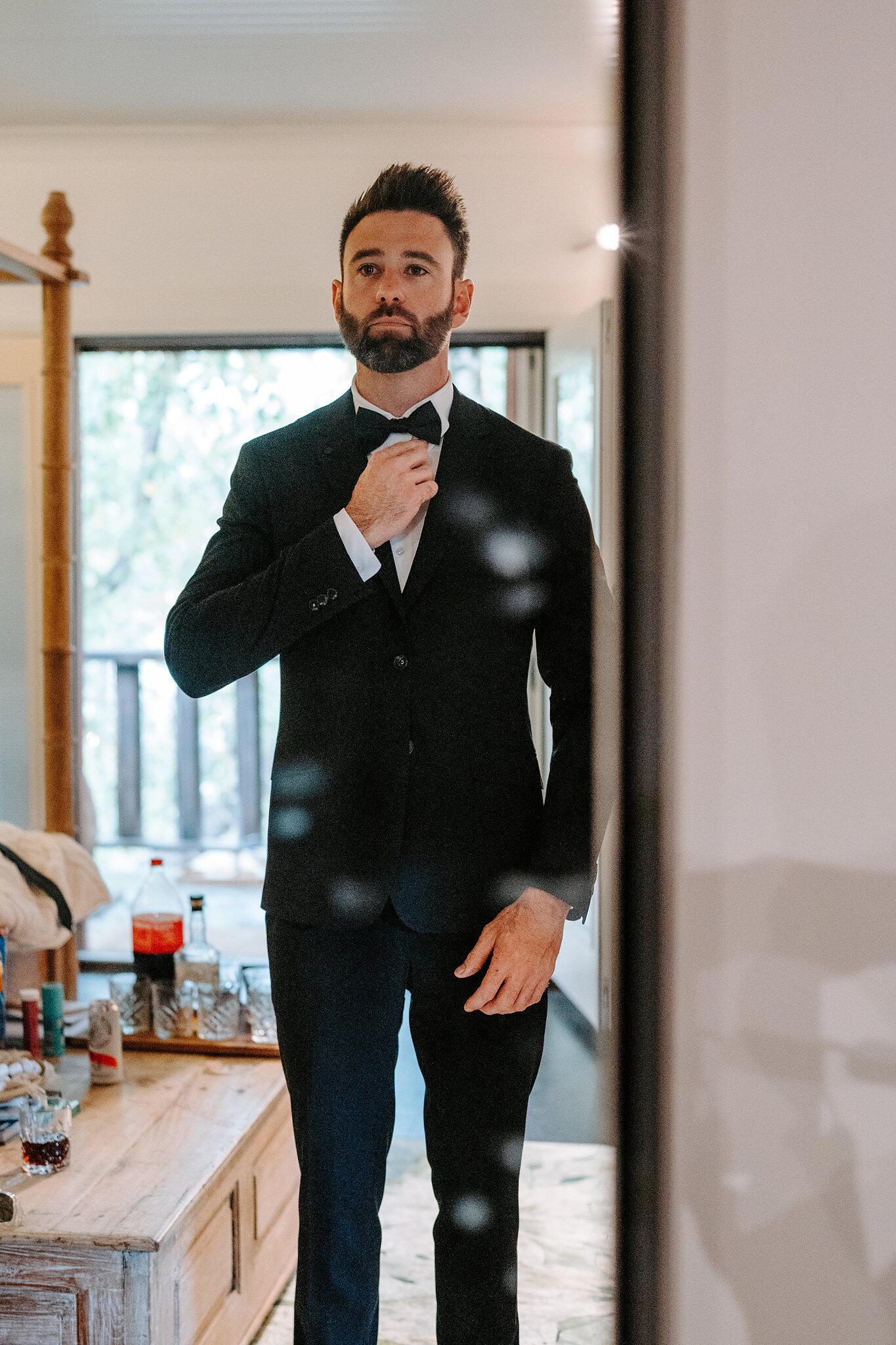 Dave straightens his bow tie in the mirror in his black tuxedo.