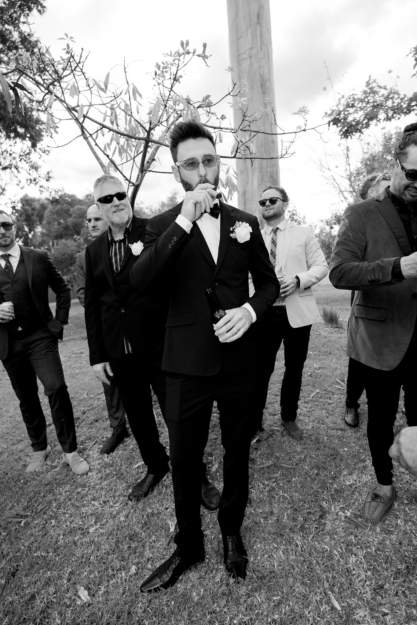 Dave sips a drink among his mates in sunglasses before the ceremony, in black and white.