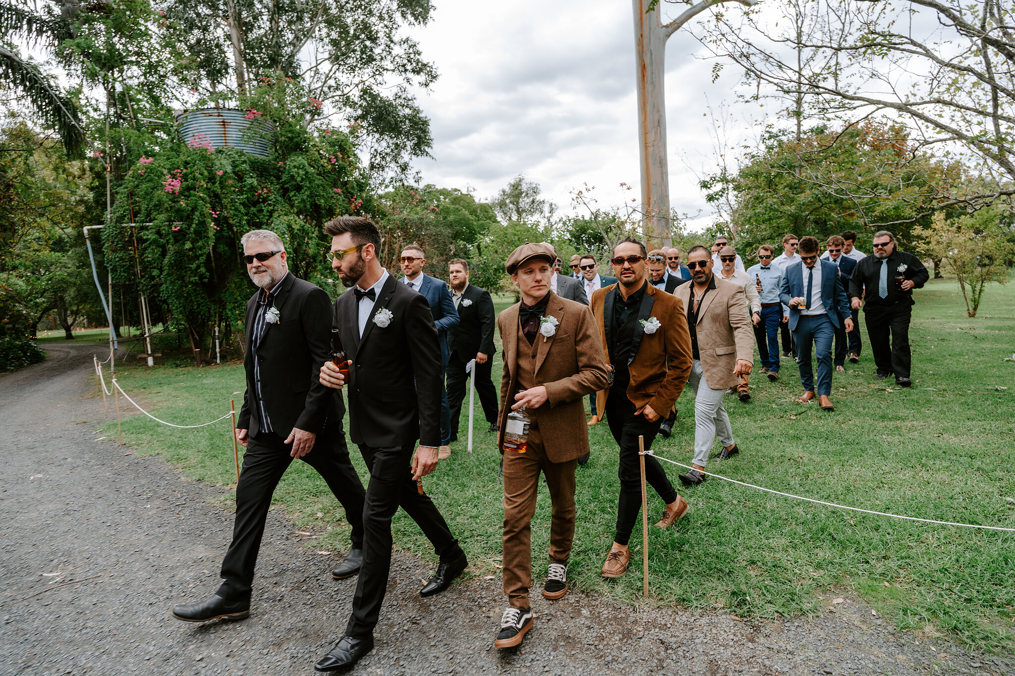Dave strides across the lawn with a crowd of mates in suits and flat caps.