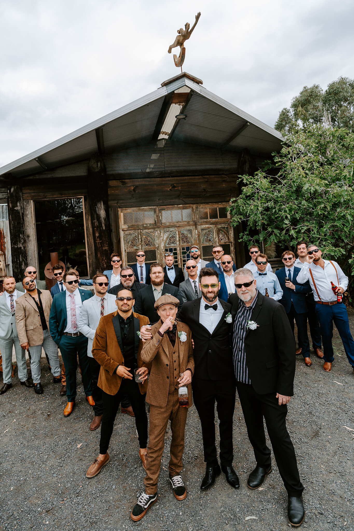 Dave and a big crowd of mates line up in front of a rustic timber shed.