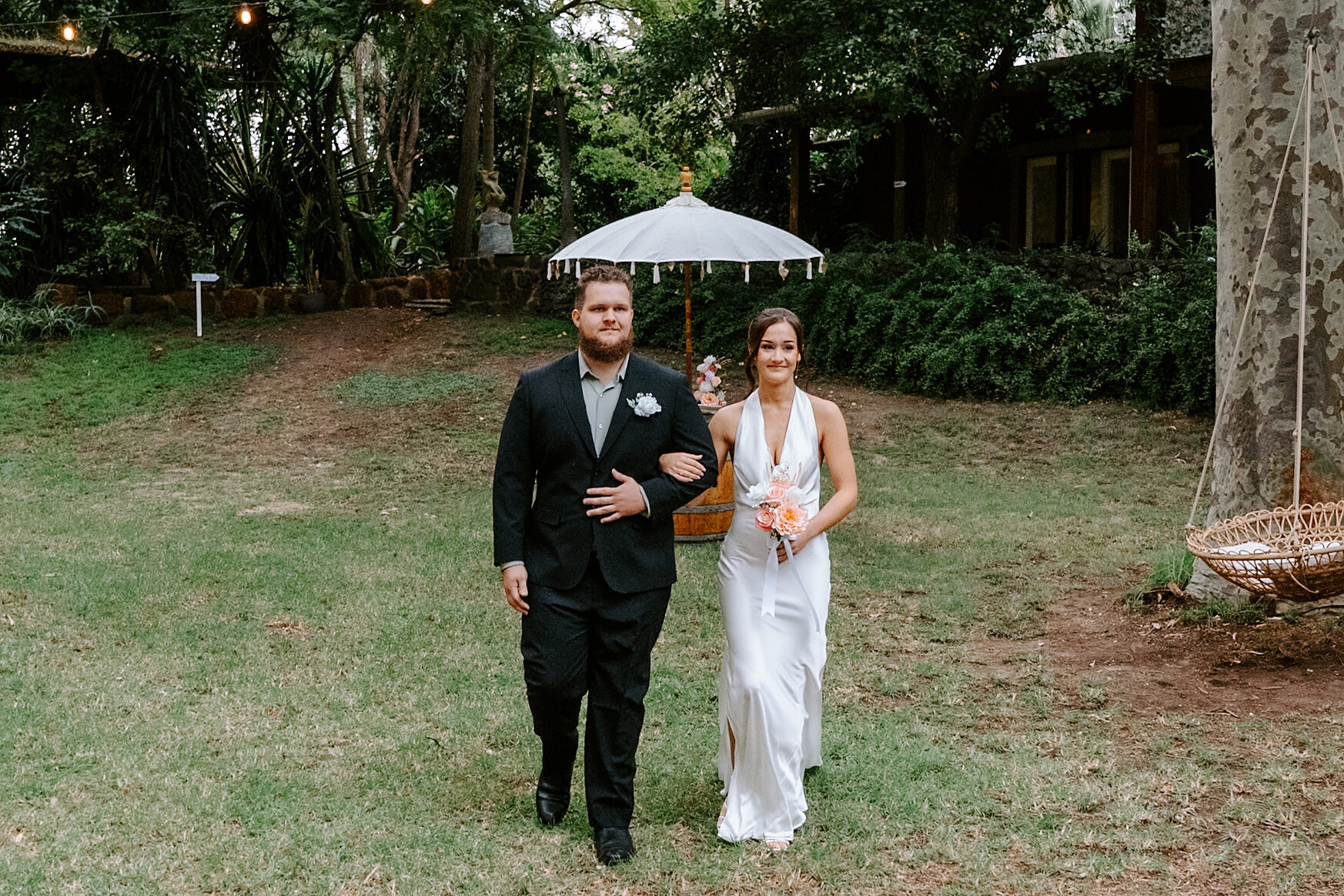 Emma’s brother walks her across the lawn past a white parasol towards the ceremony.