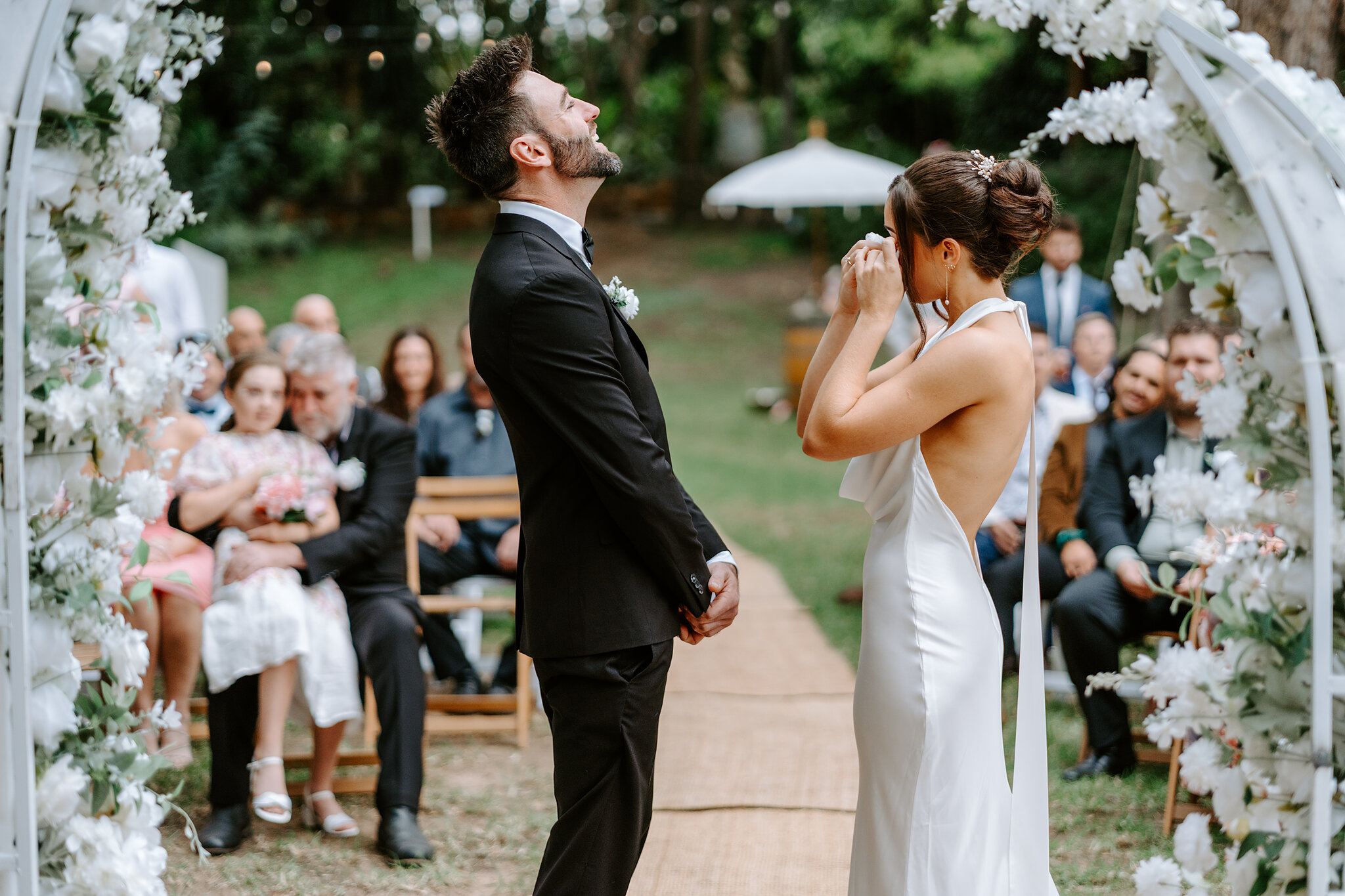 Emma wipes her eyes as Dave looks up to the sky under the floral arch.