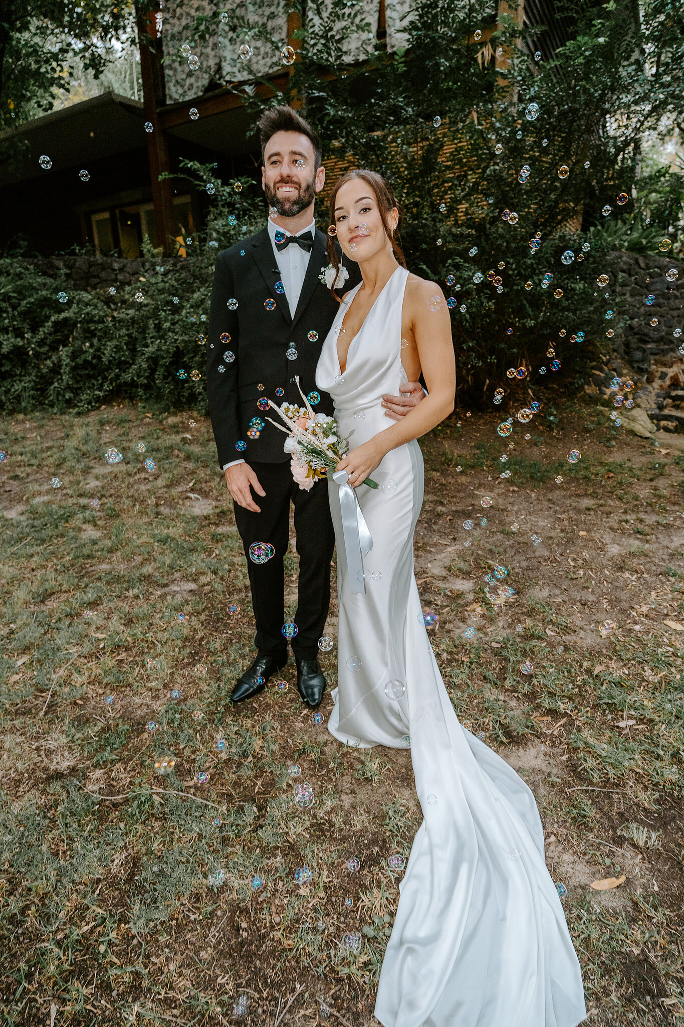Emma and Dave stand among the gums as bubbles float past, her train spread on the grass.