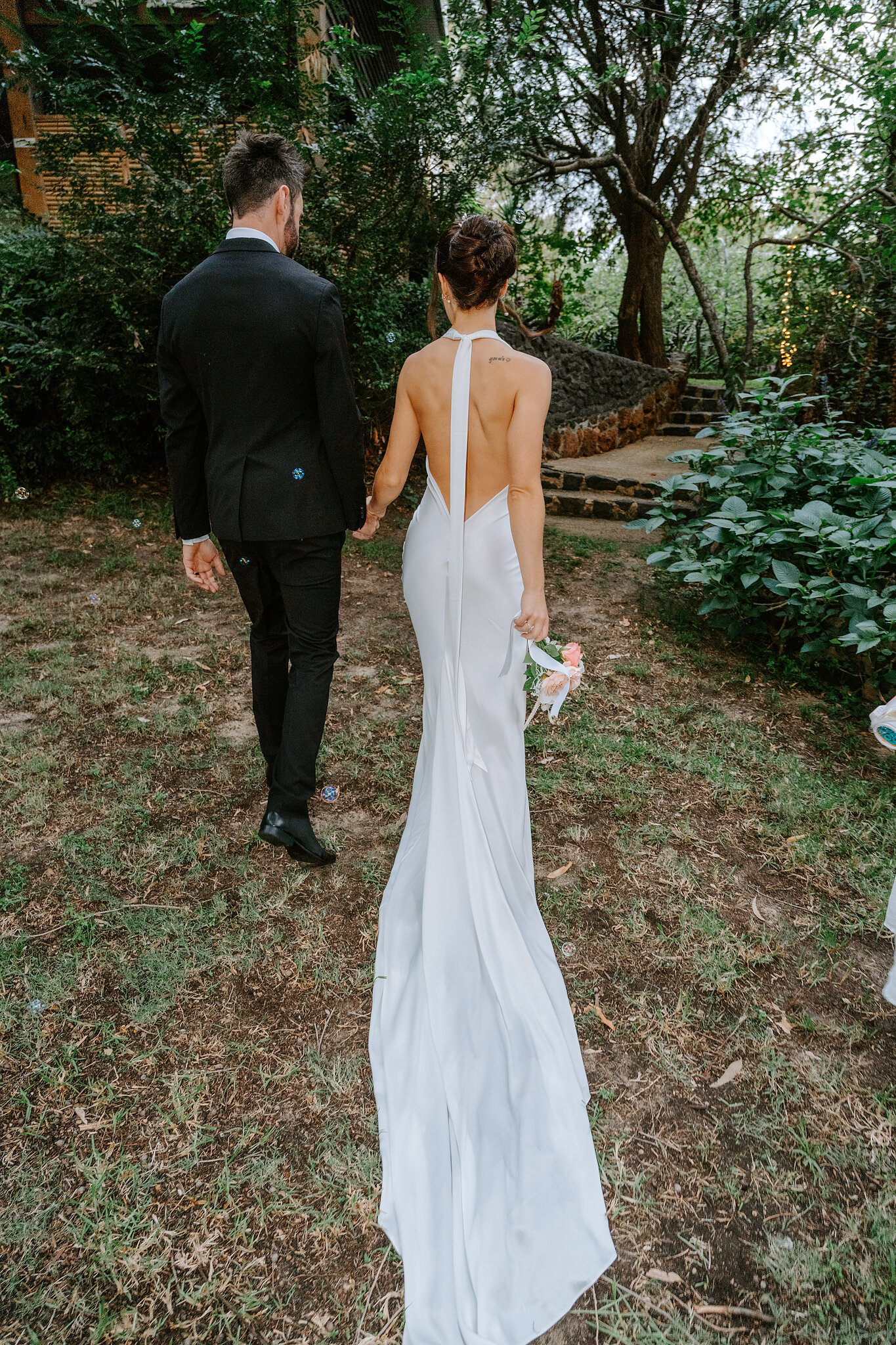 Emma and Dave walk off into the garden, her open back and train trailing behind.