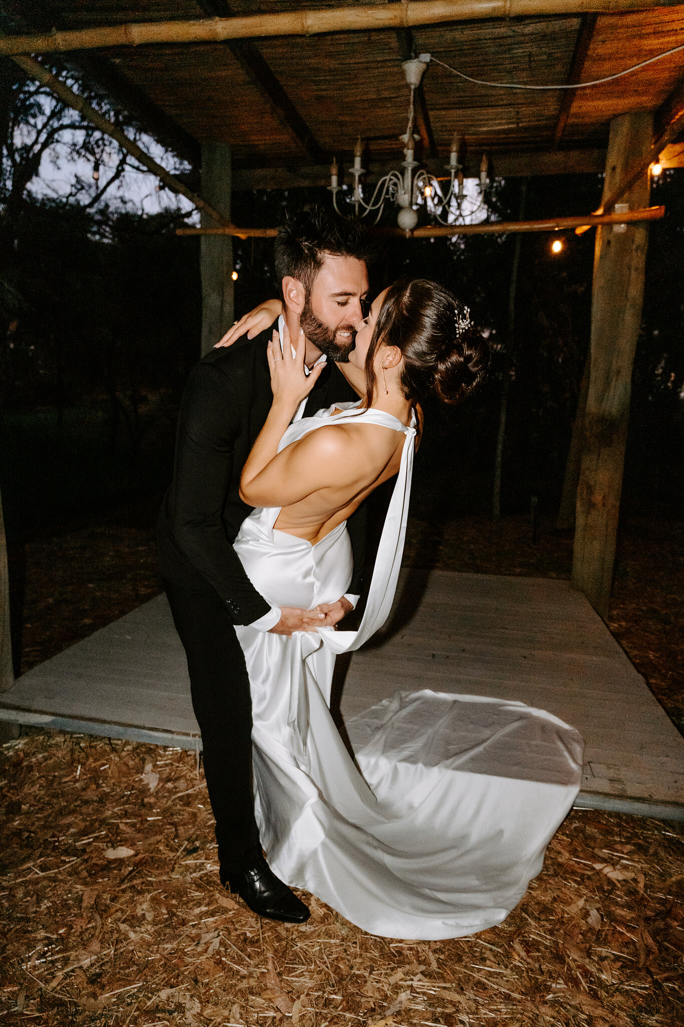 Dave dips Emma for a kiss on the timber dance floor under a chandelier.