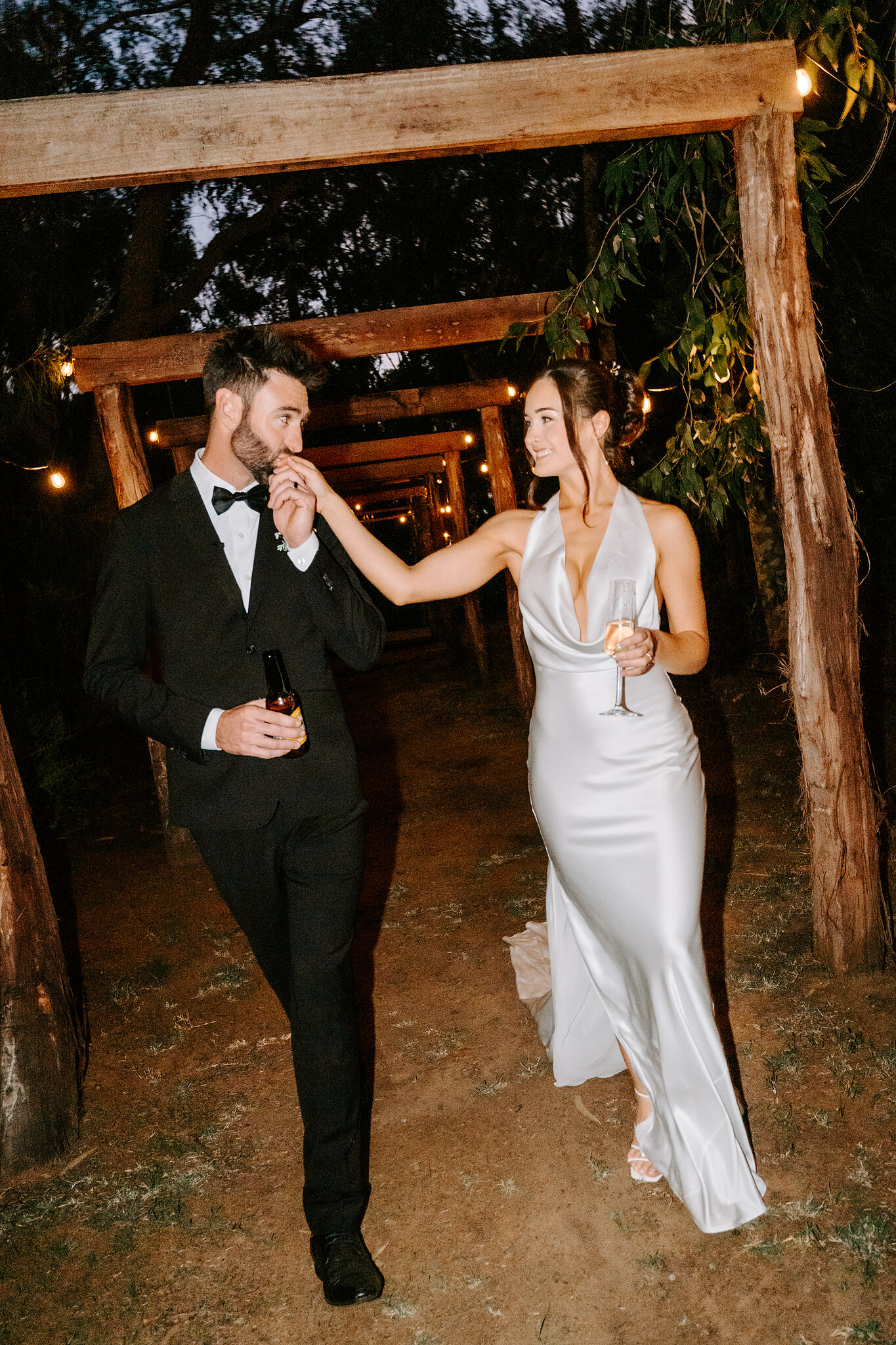Dave kisses Emma’s hand under the timber pergola walkway strung with festoon lights.