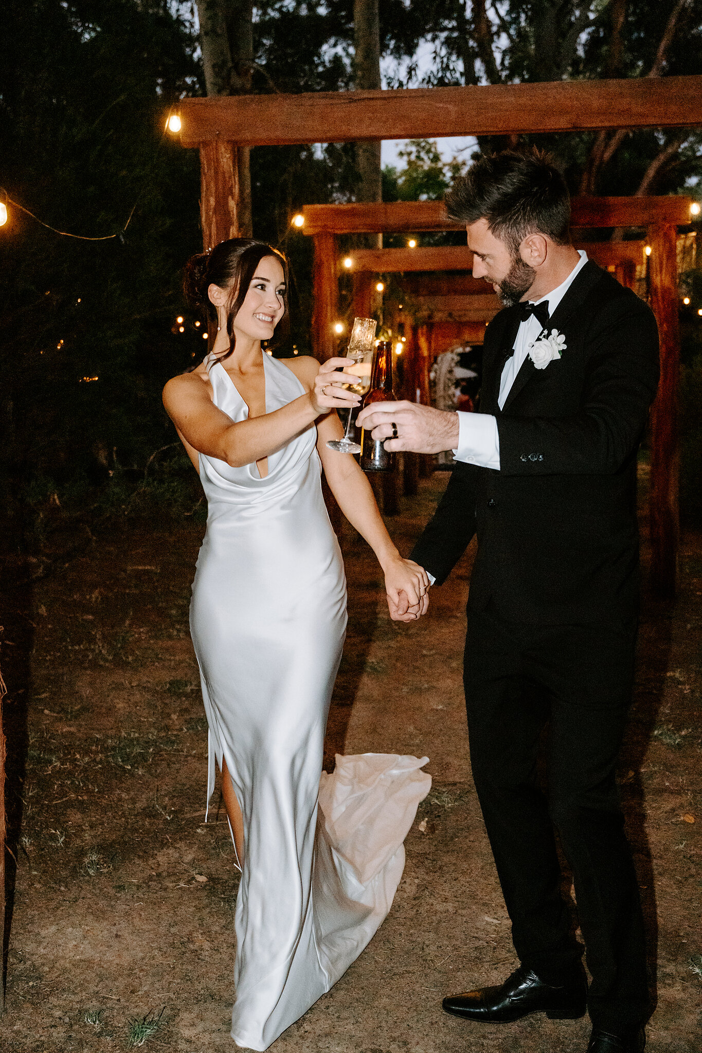 Emma and Dave clink champagne glasses under the festoon-lit timber pergola.