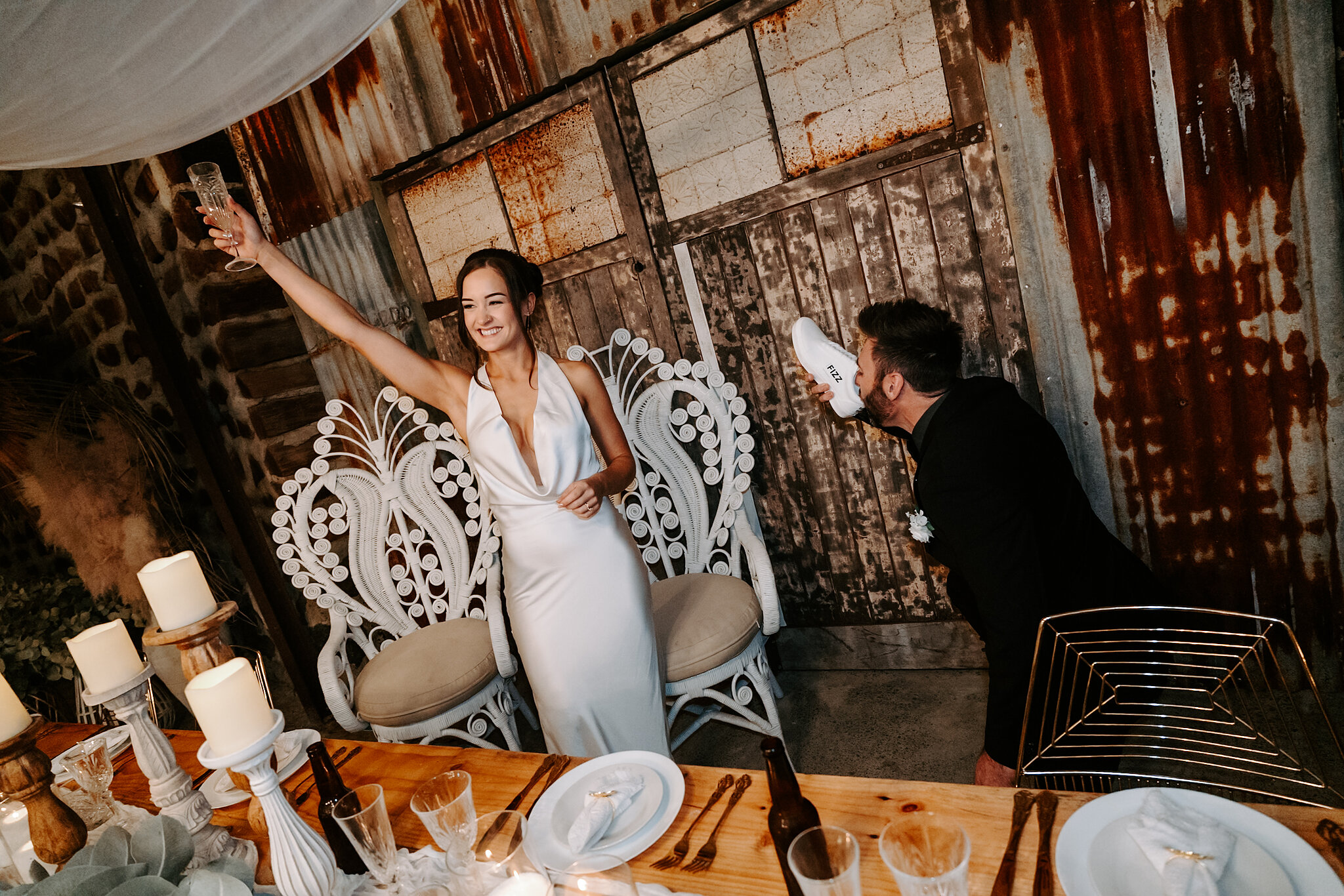 Emma raises her champagne from a peacock chair as Dave does a shoey behind her.