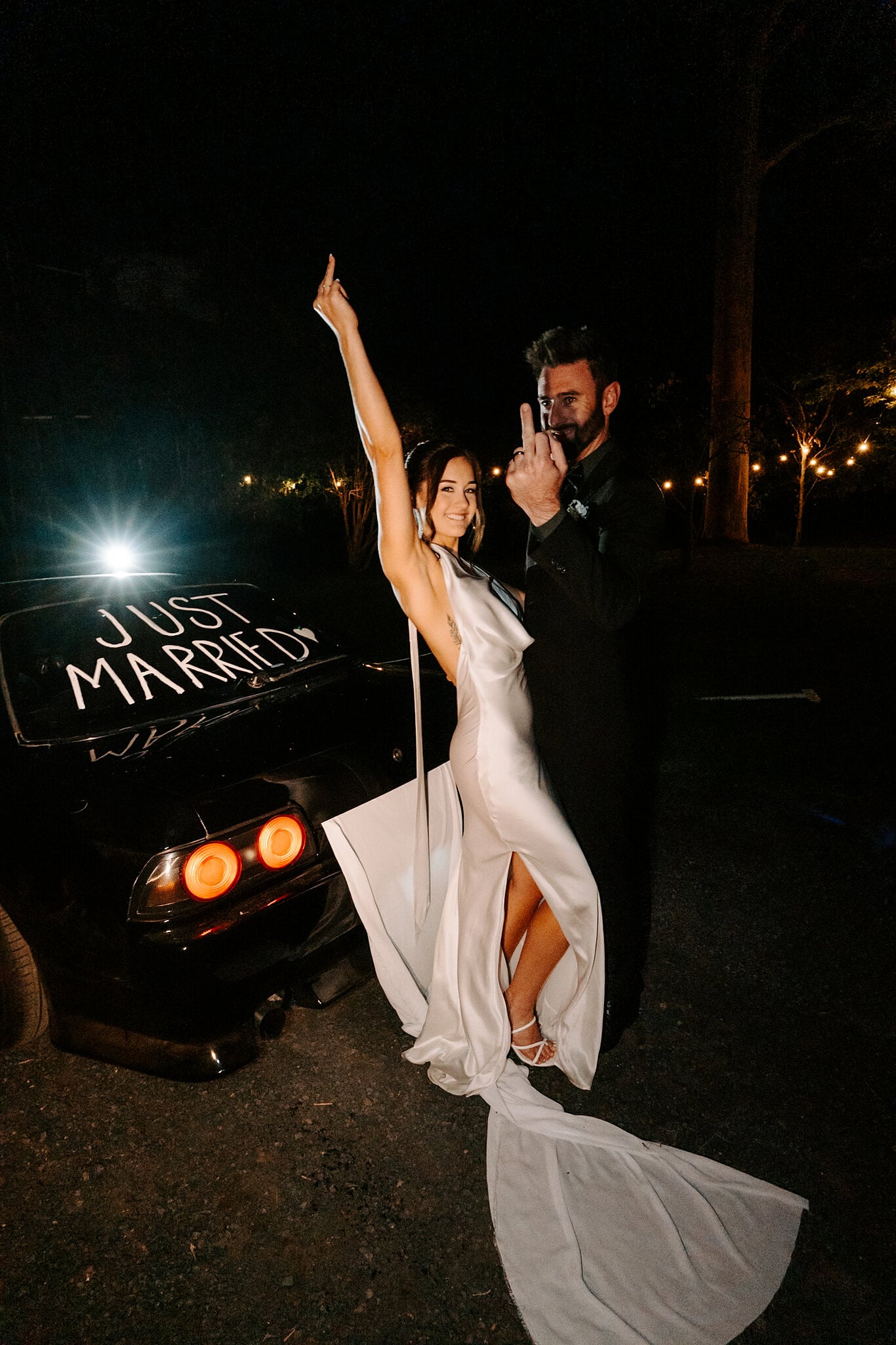 Emma throws an arm up beside a black car with Just Married written on the back window.