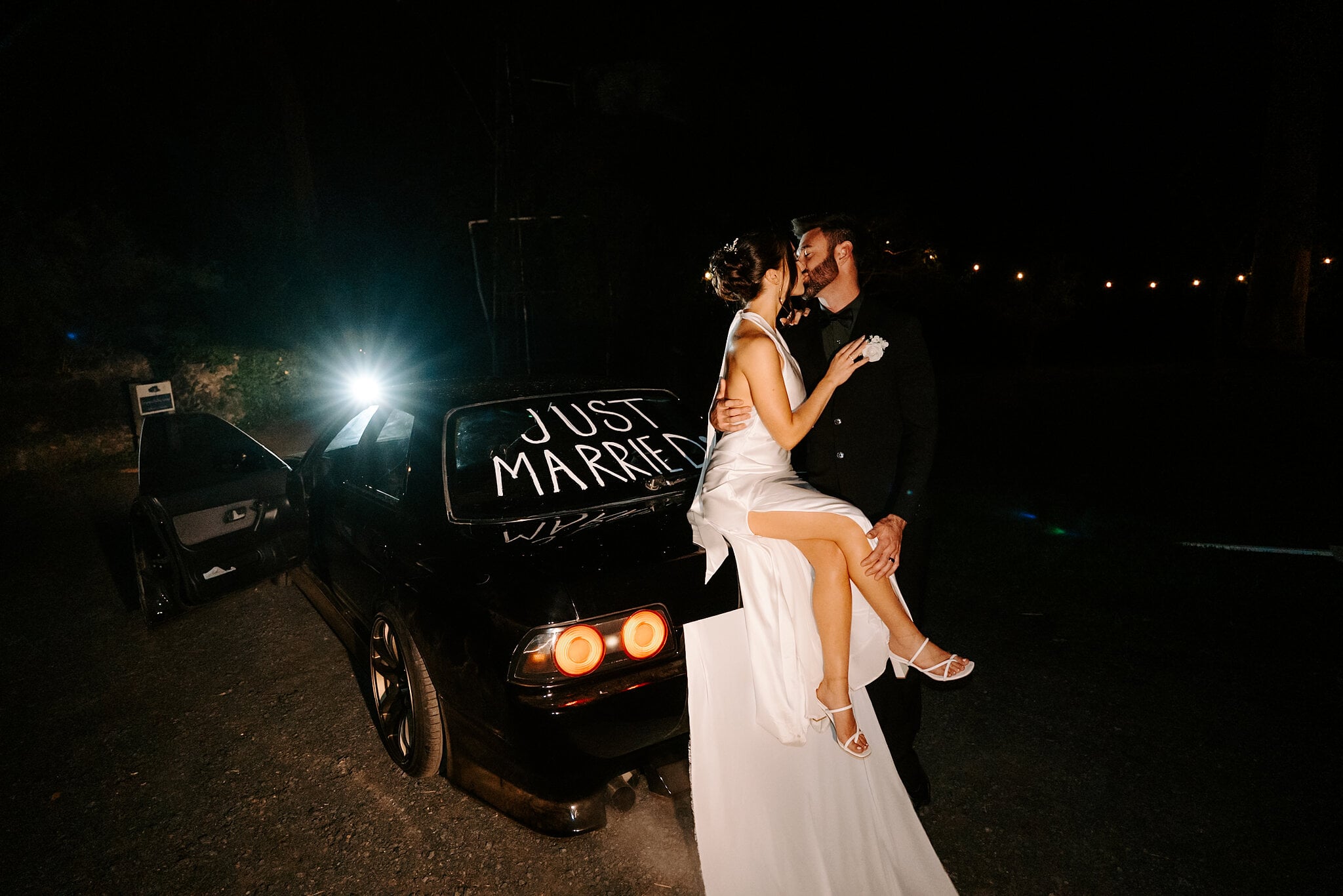 Emma sits on the back of the Just Married car, kissing Dave under the night sky.