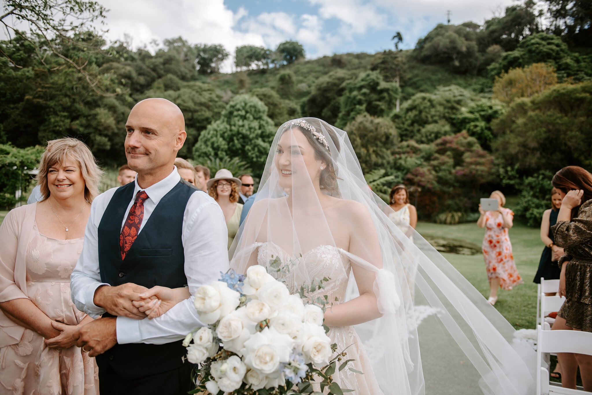 Jamie and her dad smile as they reach the front of her garden ceremony.