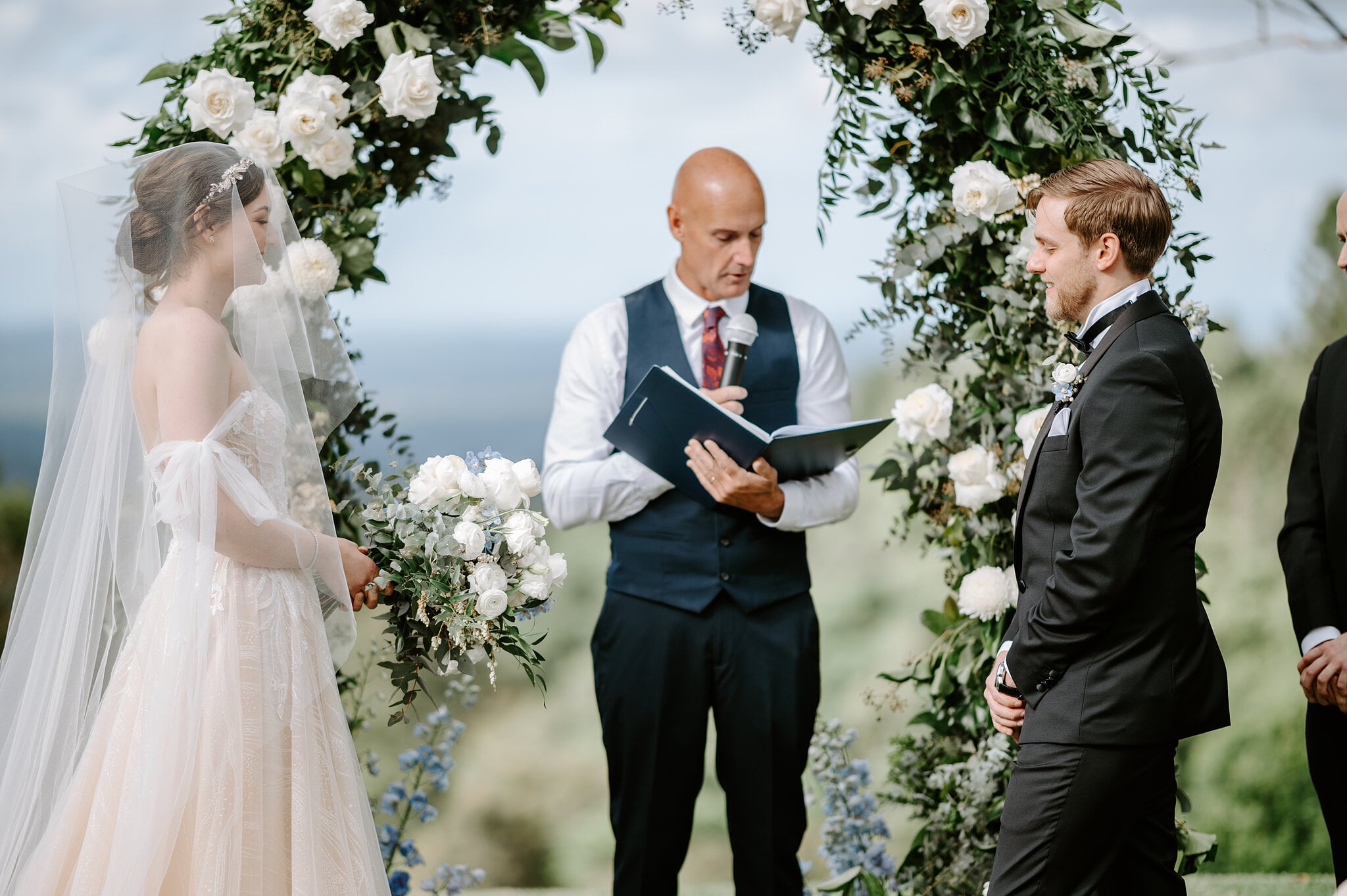 Jamie’s dad leads the ceremony under the rose arch as Jamie and Tim face each other, the ocean on the horizon.