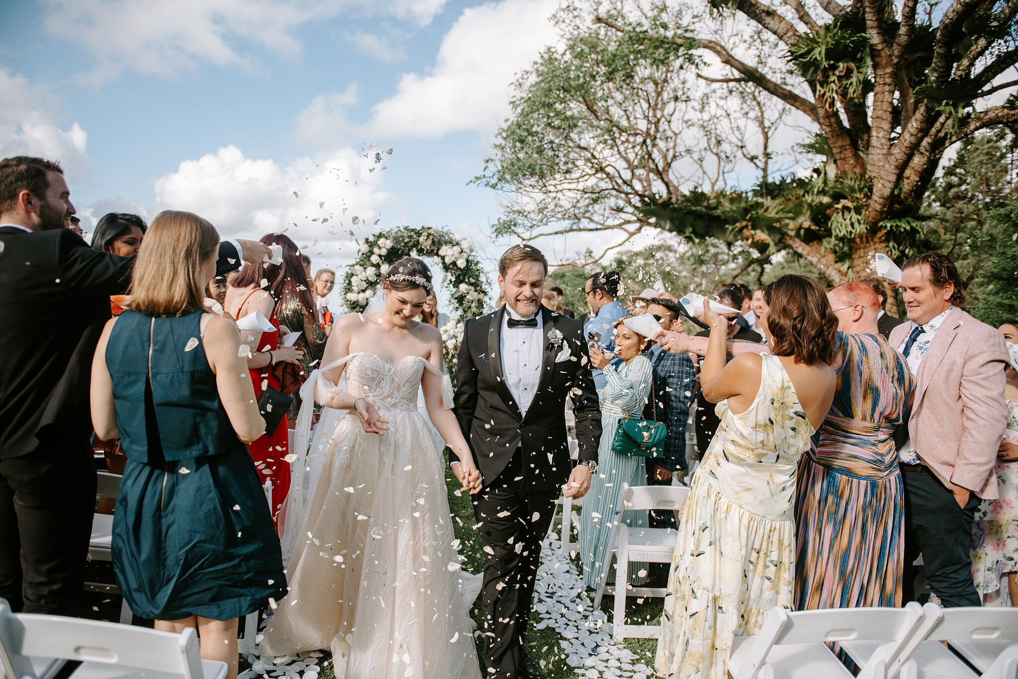 Guests throw petals as Jamie and Tim walk back down the aisle beneath the spreading Crow’s Ash tree.