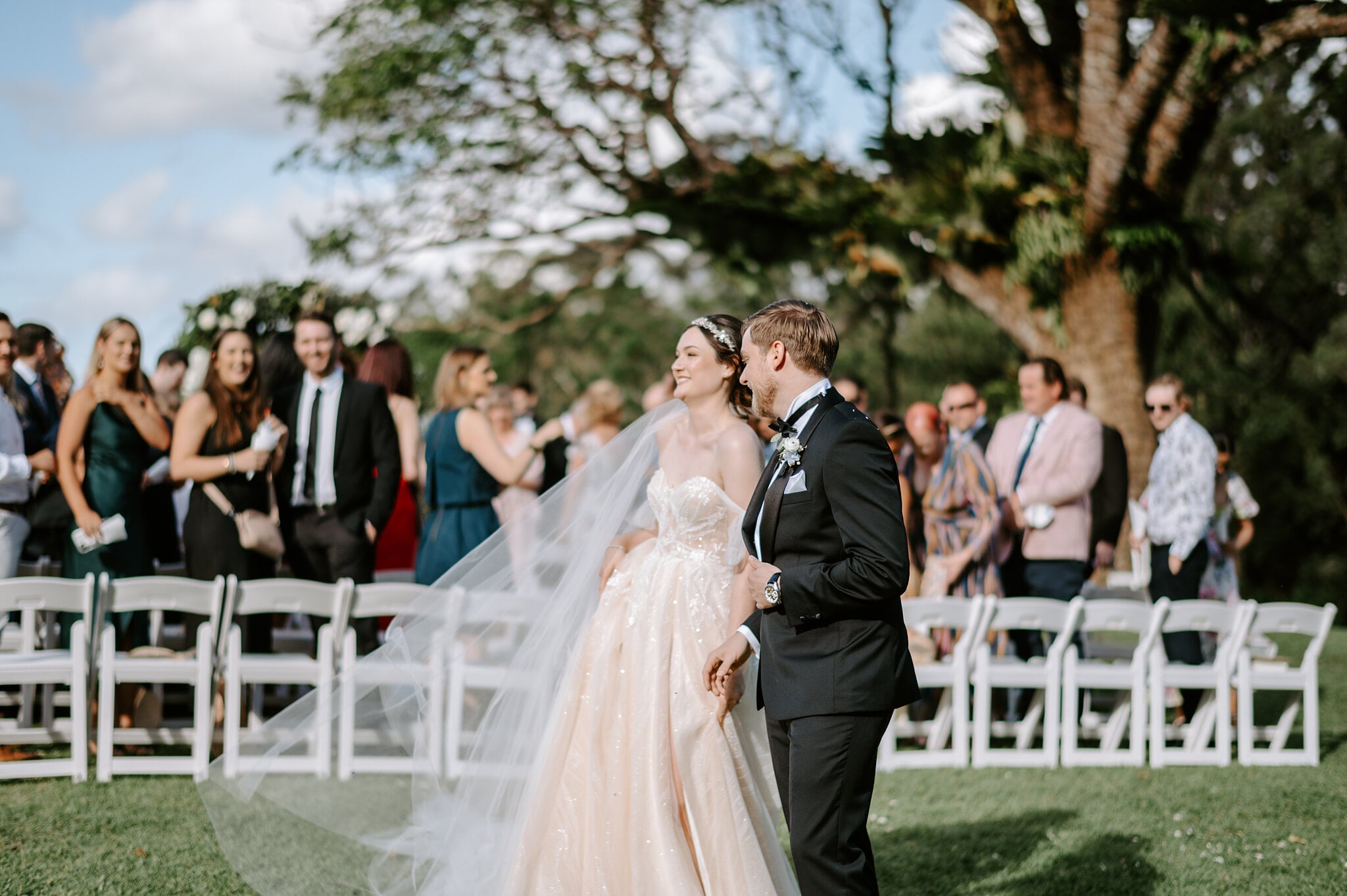 Jamie and Tim laugh past the white chairs as their guests cheer.