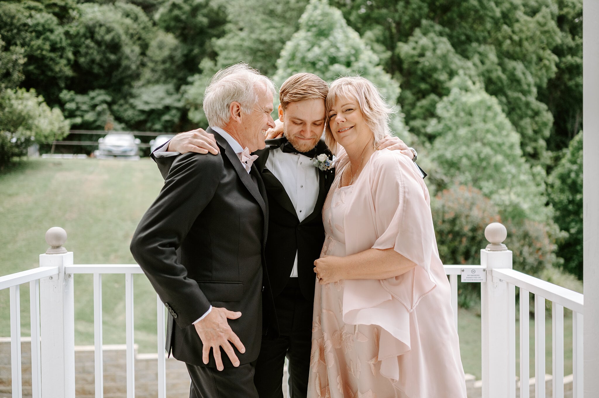 Tim hugs his mum and dad on the Maleny Manor veranda, the lawn and pines behind them.