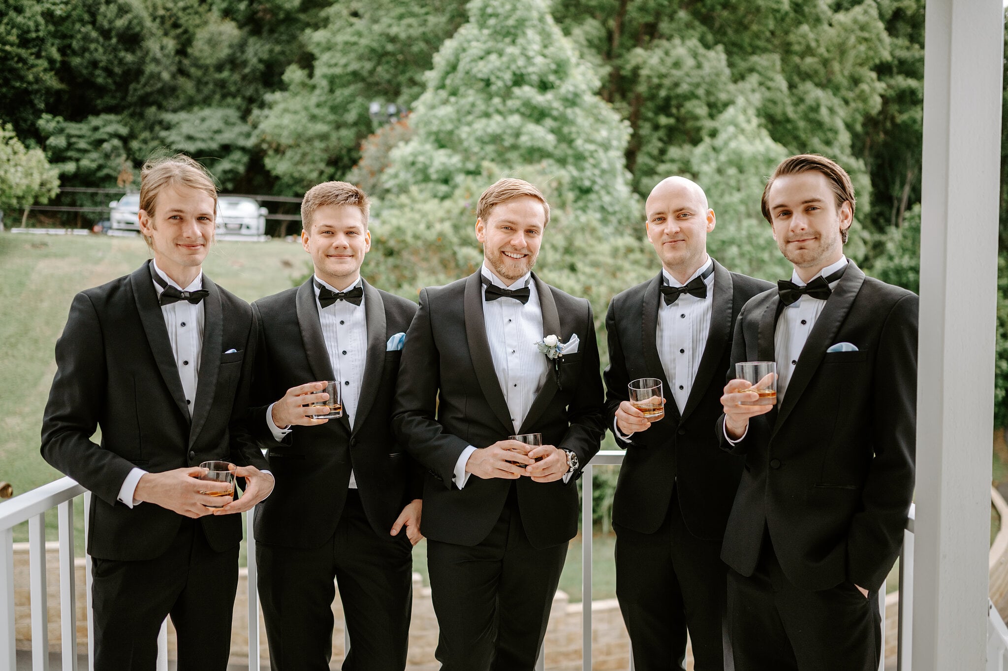 Tim and his four groomsmen in black tie raise glasses of whisky on the white veranda at Maleny Manor.