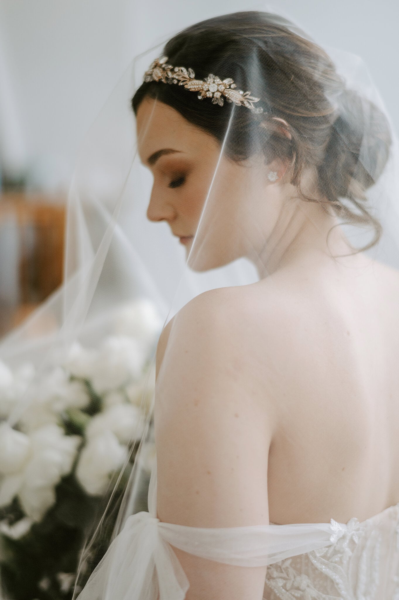 Jamie looks down through her veil, a crystal hair vine catching the window light.