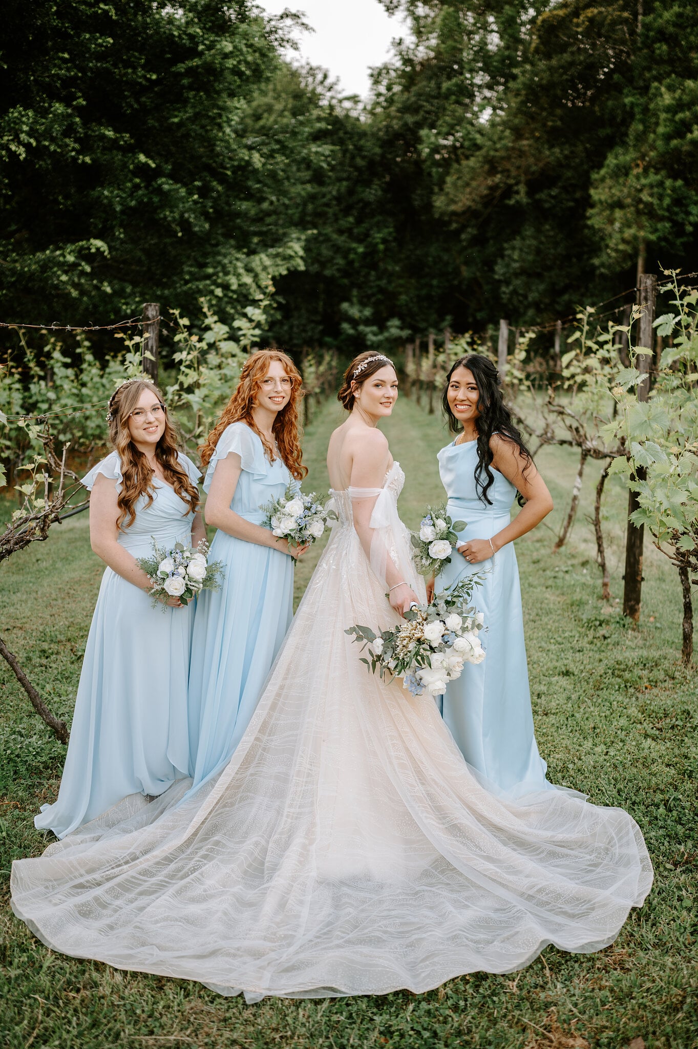 Jamie stands among the grapevines with her bridesmaids, her long train fanned out on the grass.