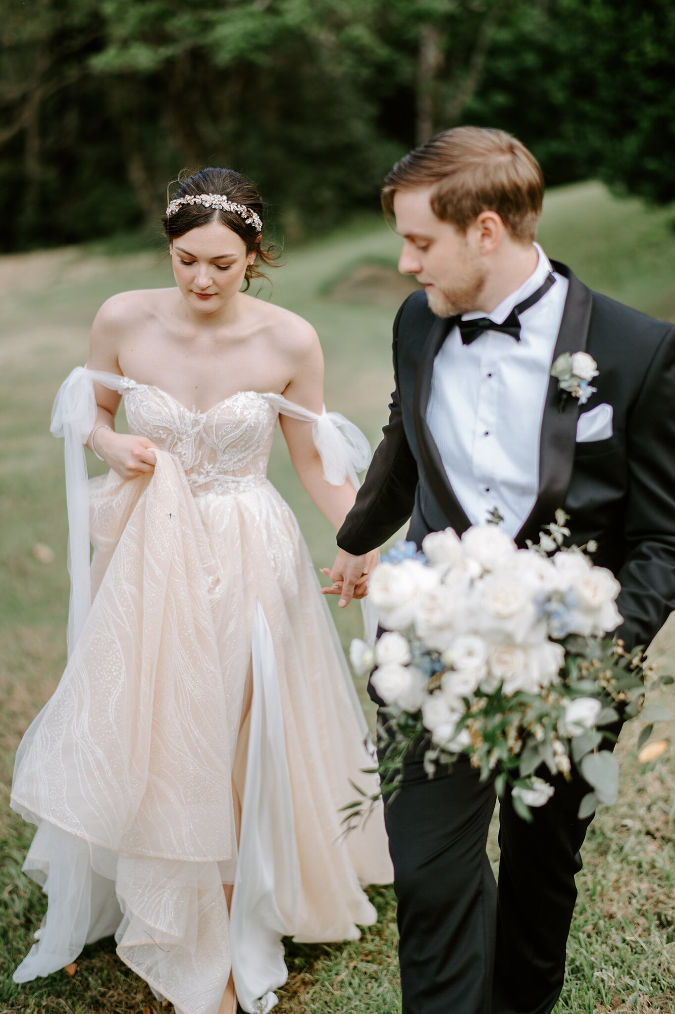 Jamie lifts her skirt as she and Tim walk down a grassy slope, Tim carrying her bouquet.