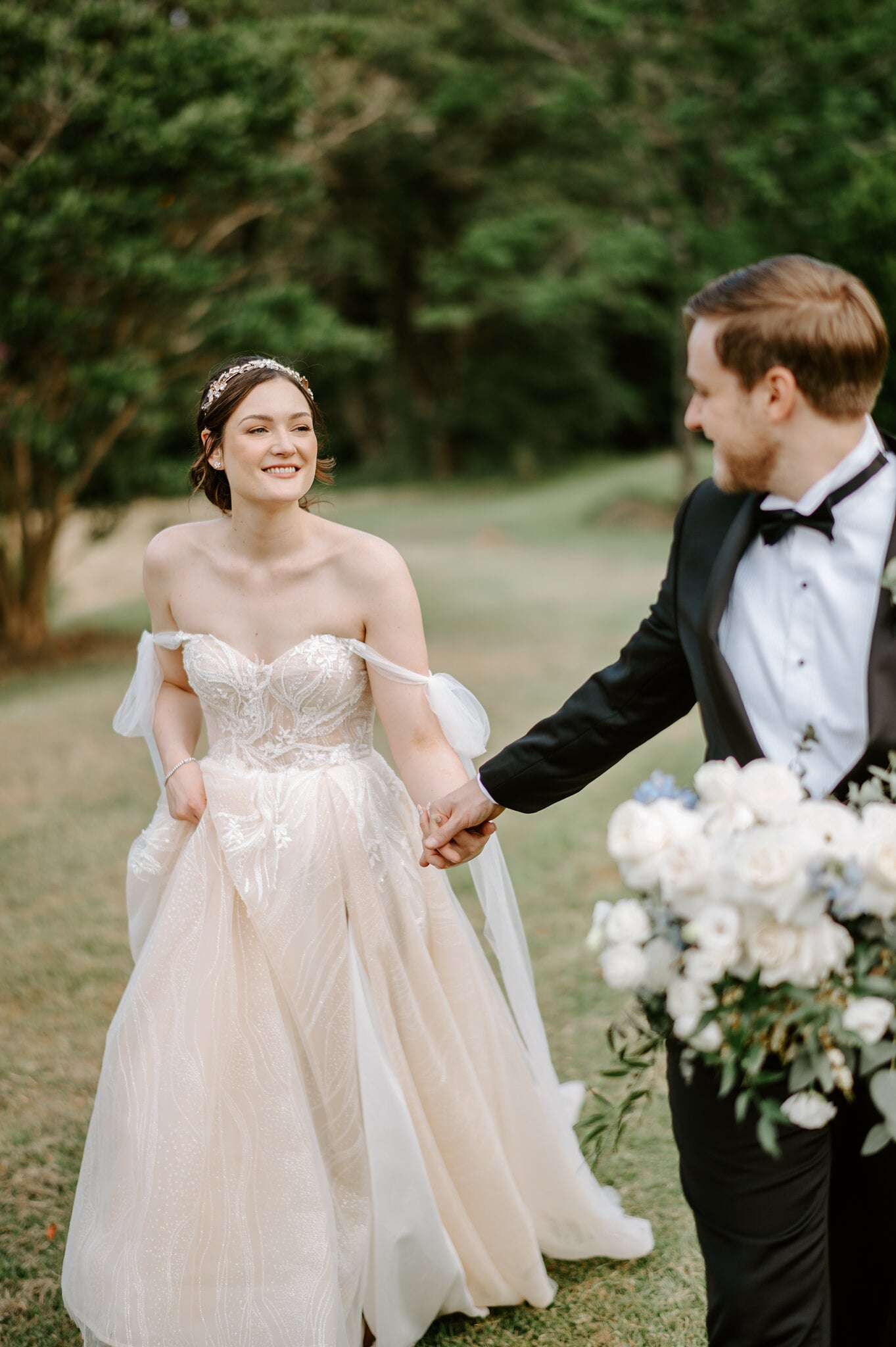 Jamie laughs as she leads Tim across the grass by the hand, white roses in his other hand.