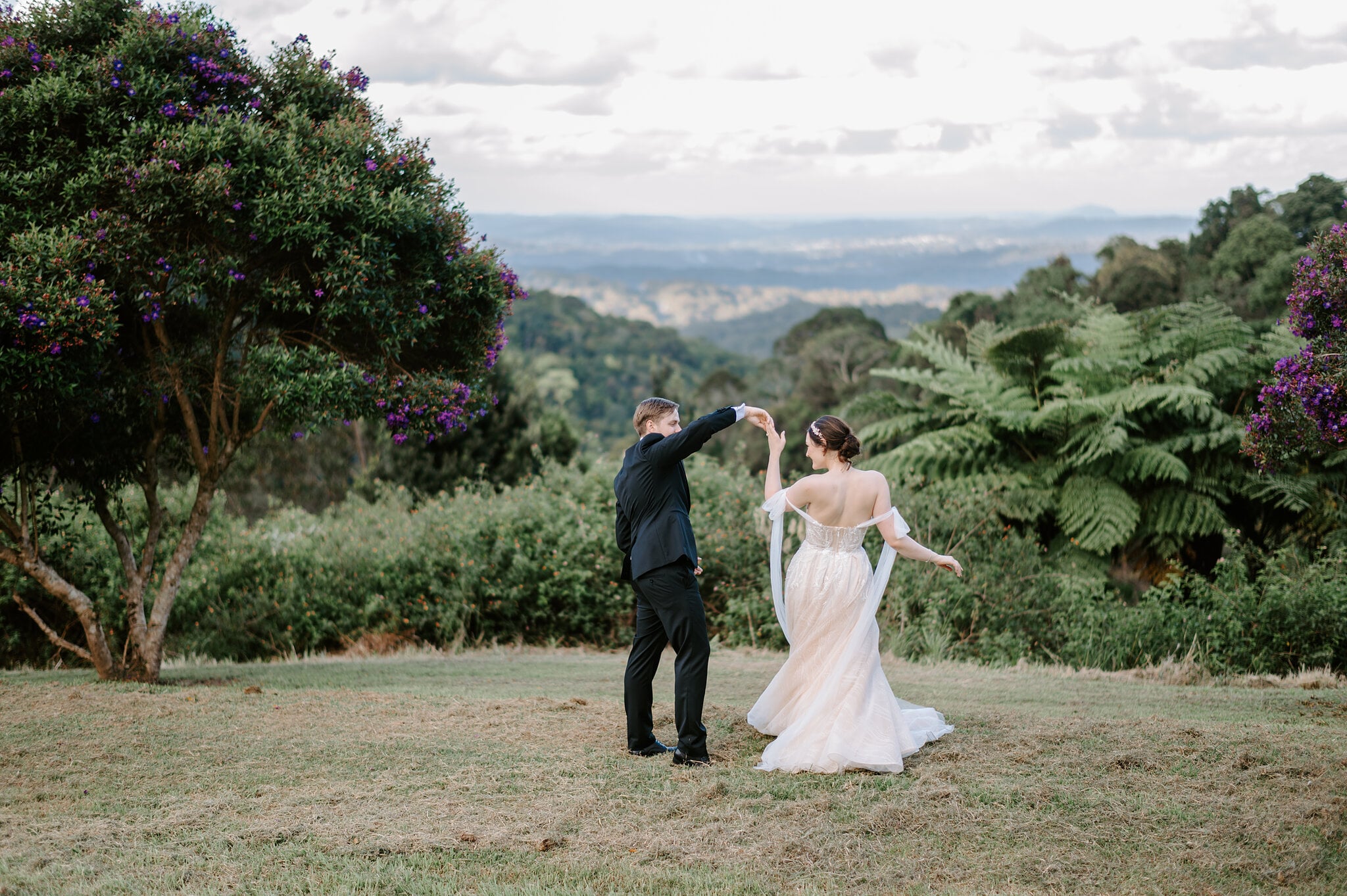 Tim twirls Jamie on the hilltop lawn at Maleny Manor, tree ferns and purple blooms framing the view to the coast.