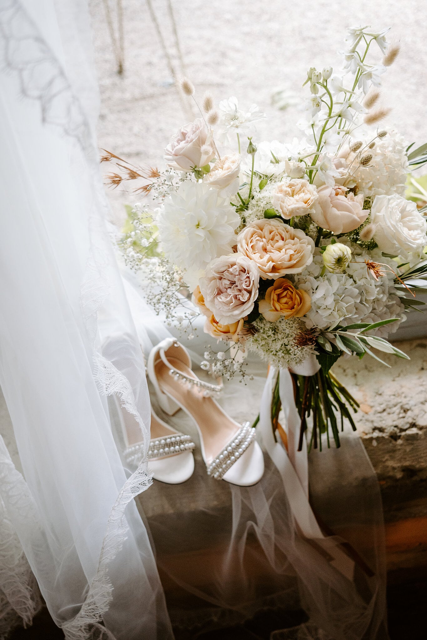 Peach and blush roses, dahlias and bunny tails in Samantha’s bouquet beside her pearl-strapped heels.