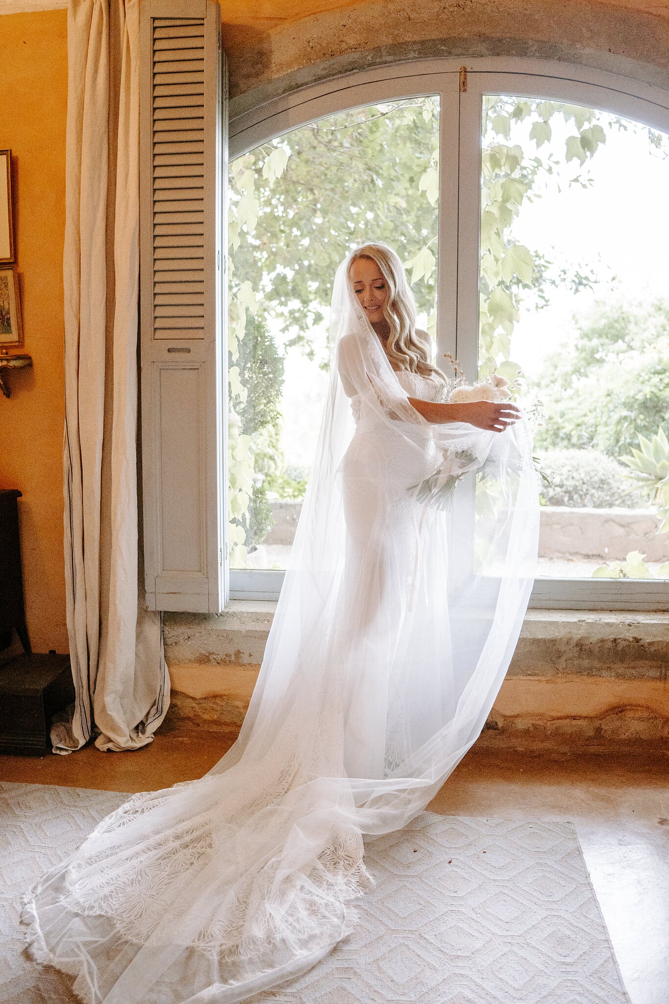 Samantha twirls her long veil across the rug by the arched cottage window.