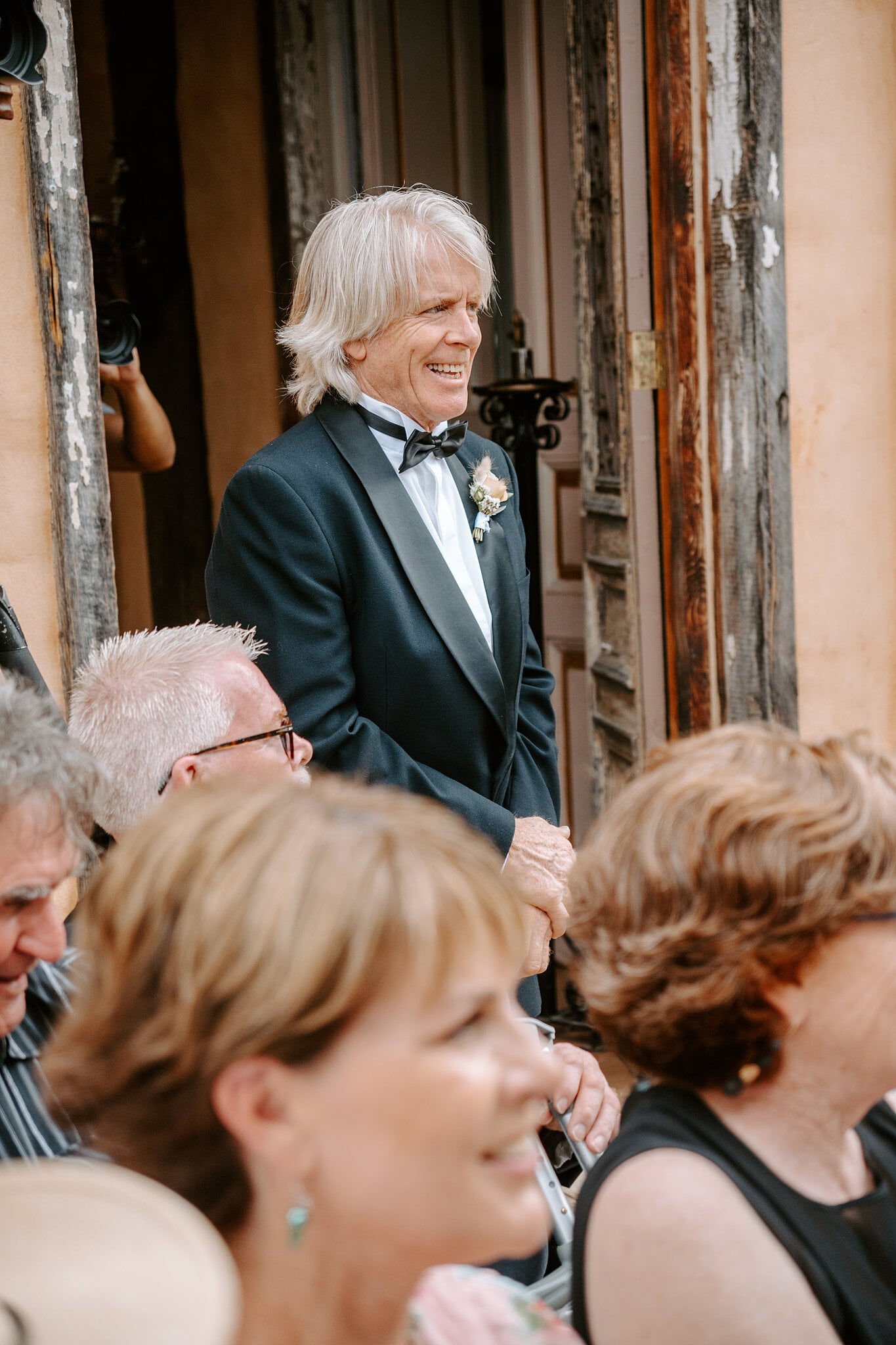 Samantha’s dad, in a tuxedo, beams during the ceremony beside the old timber doorway.