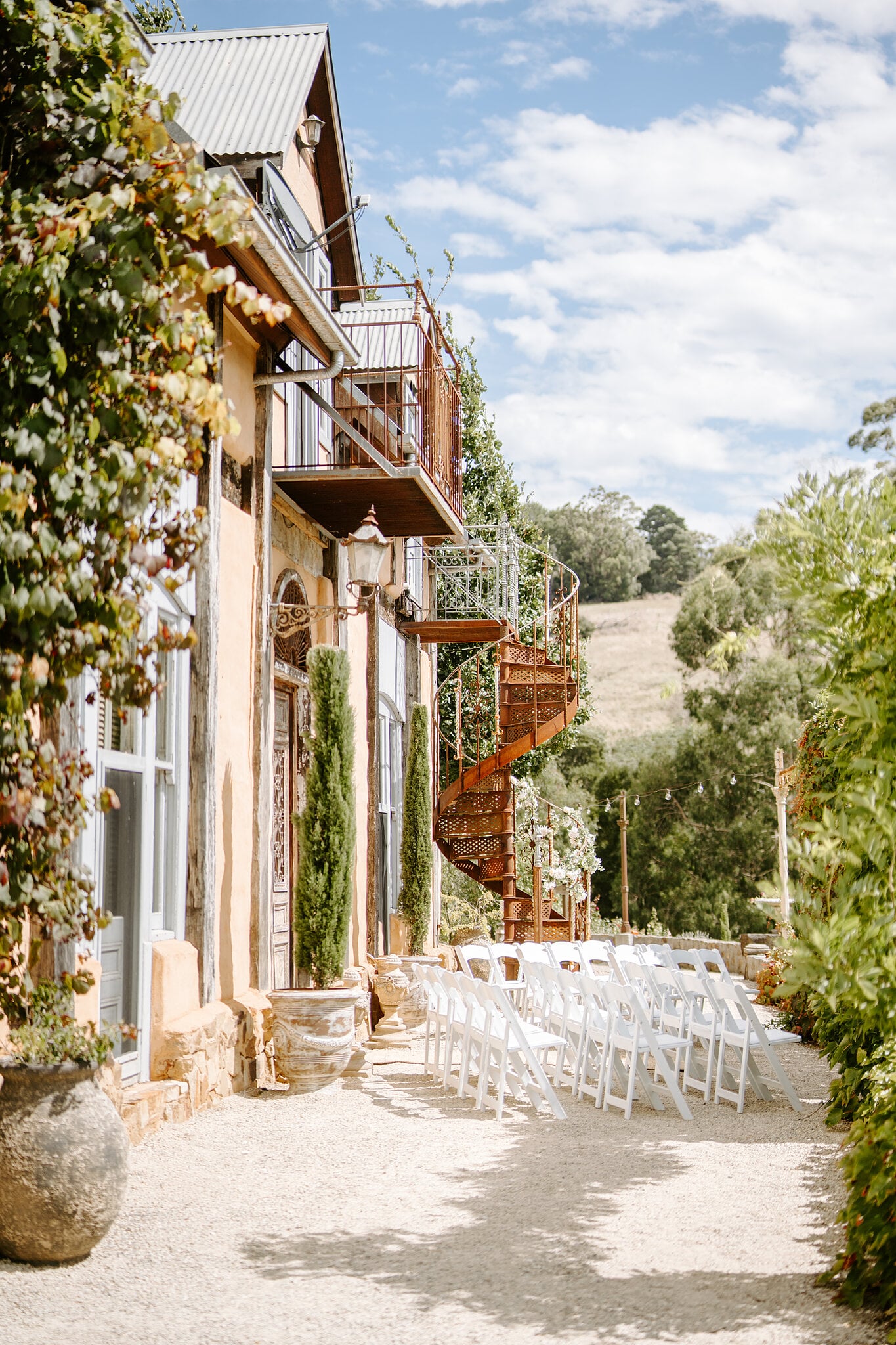 Vine-covered walls, iron balconies and a rust-red spiral staircase above the ceremony chairs at Mont du Soleil.