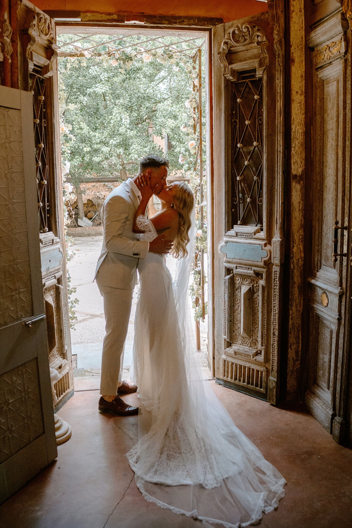 Samantha and Harrison kiss in the doorway between two carved timber doors.