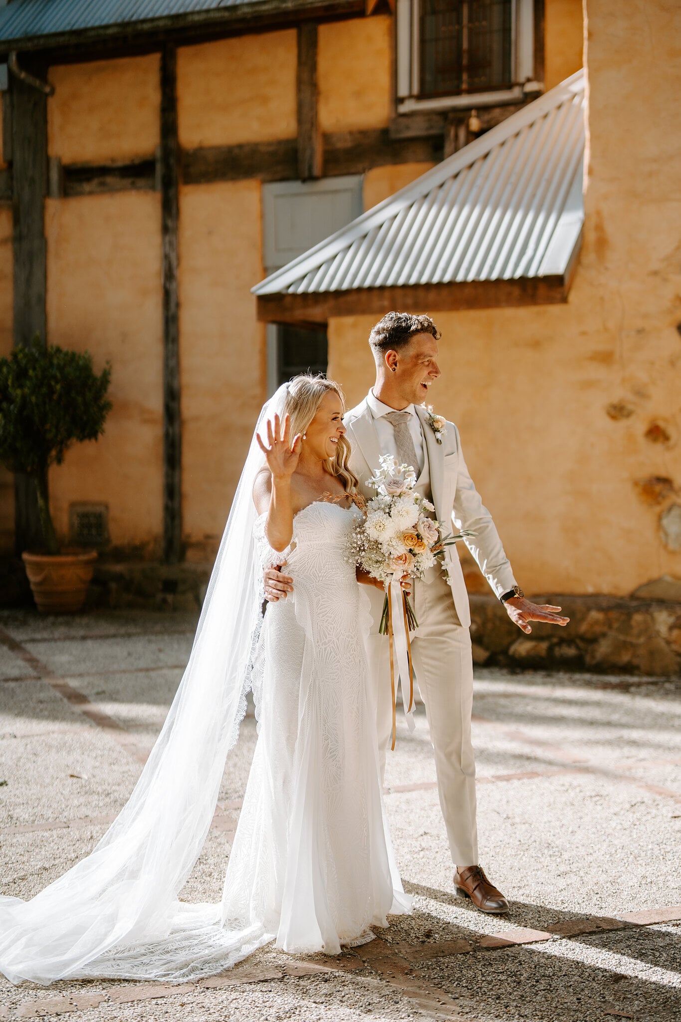 Samantha waves as she and Harrison stroll past the ochre walls of the courtyard.